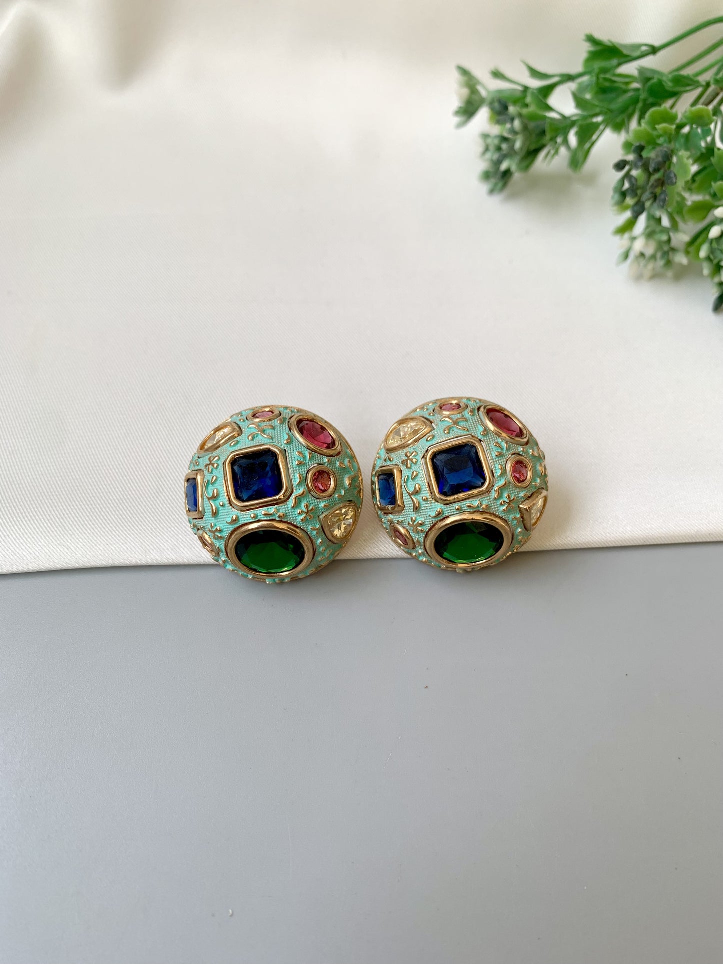 Colorful gemstone earrings on a white surface with green leaves in the background