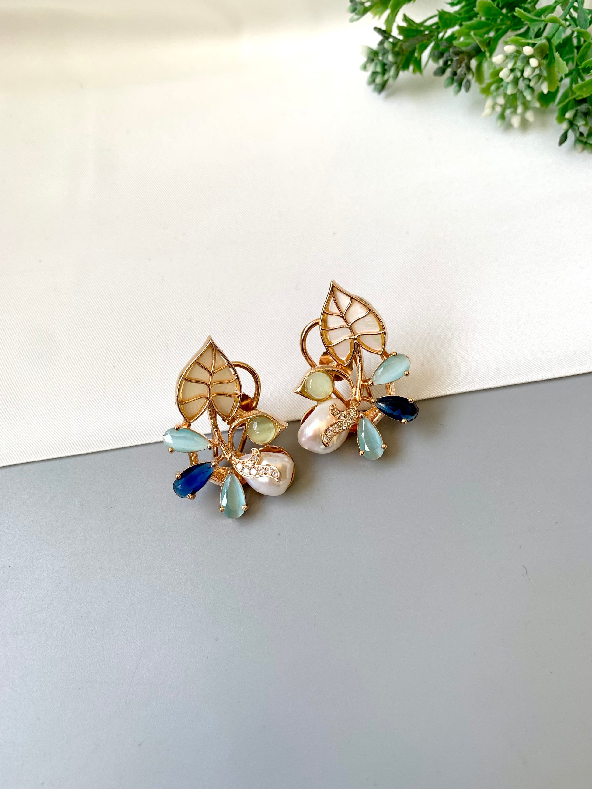 Pair of gold earrings with gemstones on a reflective surface