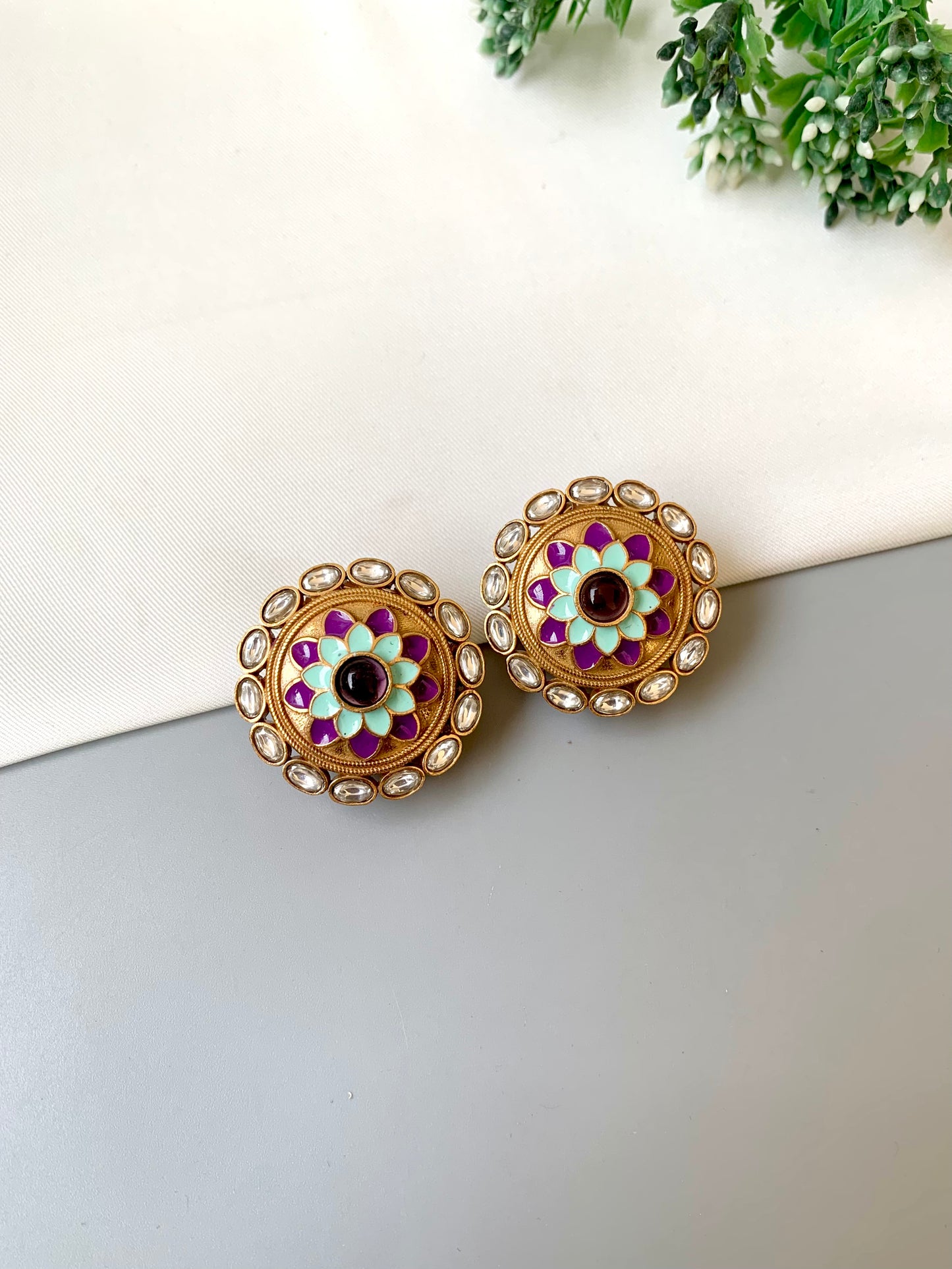 Pair of decorative earrings on a white surface with greenery in the background