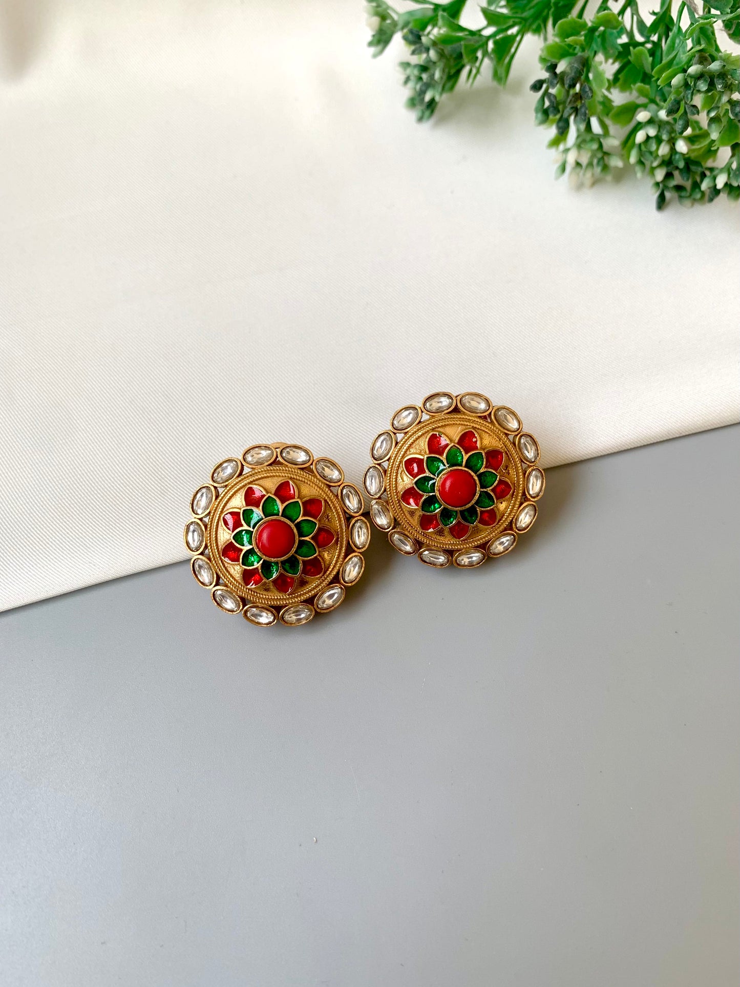 Pair of gold earrings with red and green accents on a white surface.