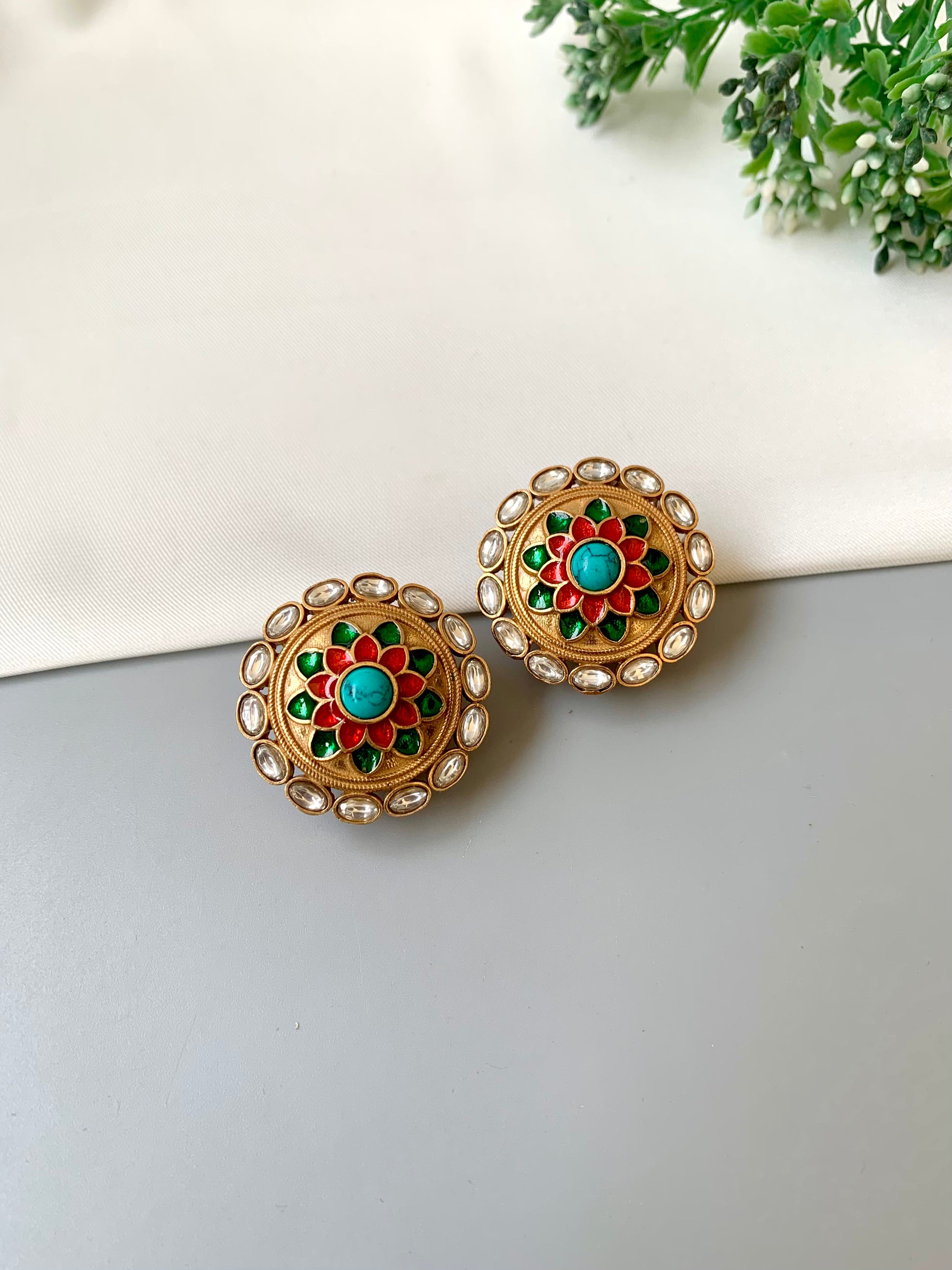 Pair of gold earrings with turquoise and red stones on a white surface.