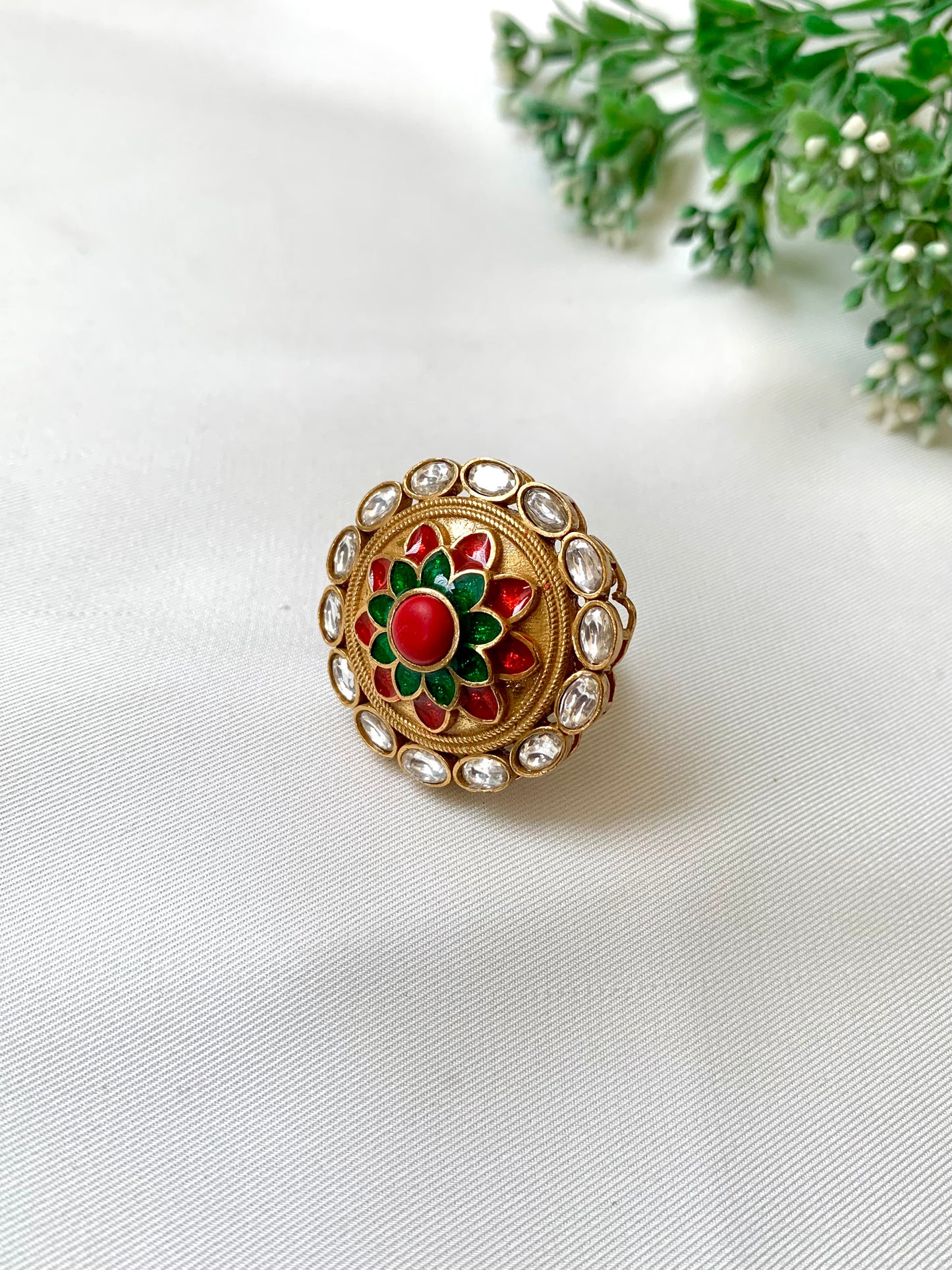Decorative ring with red and green gemstones on a white fabric background