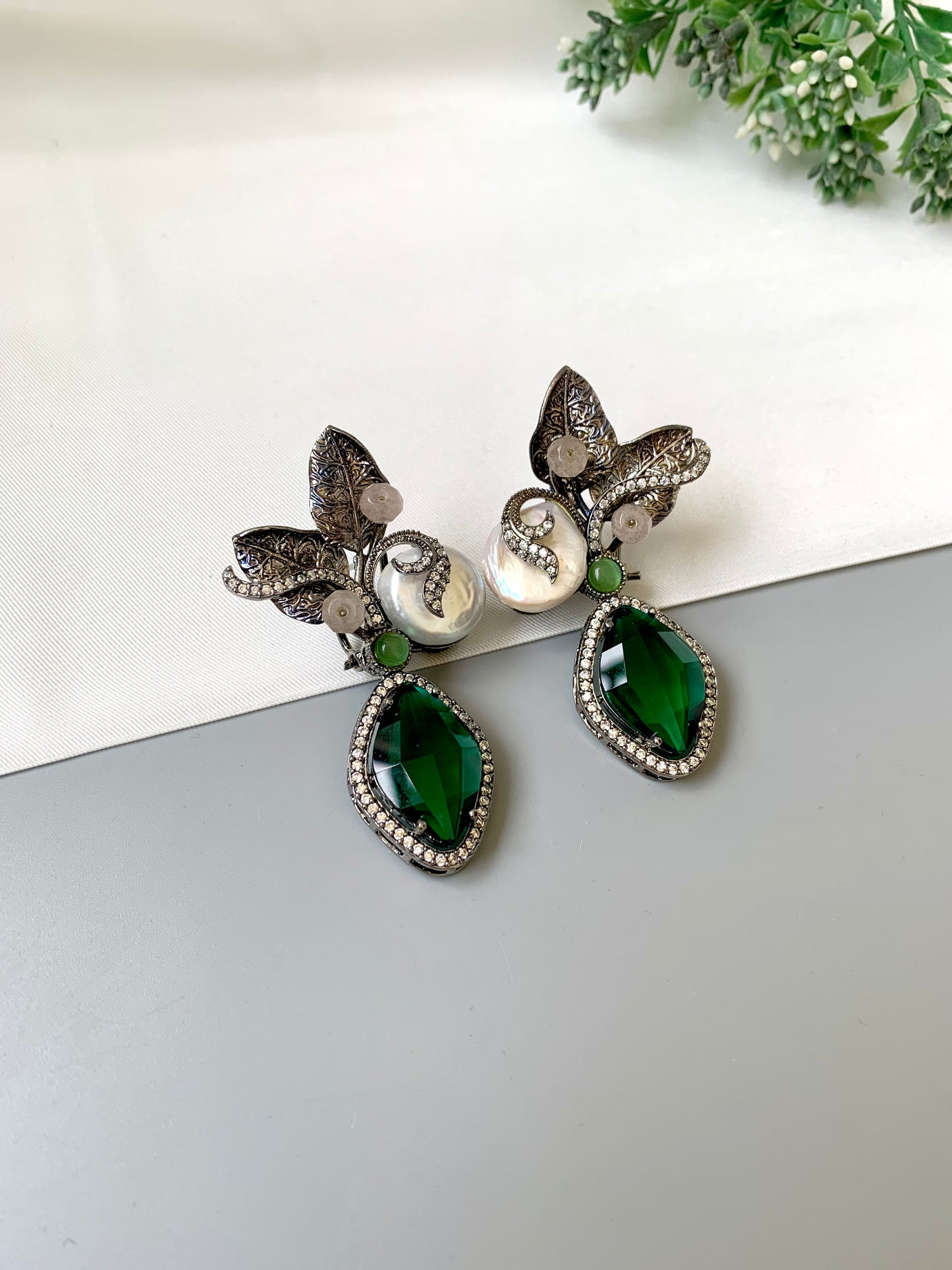 Pair of earrings with green teardrop stones and butterfly designs on a white surface.