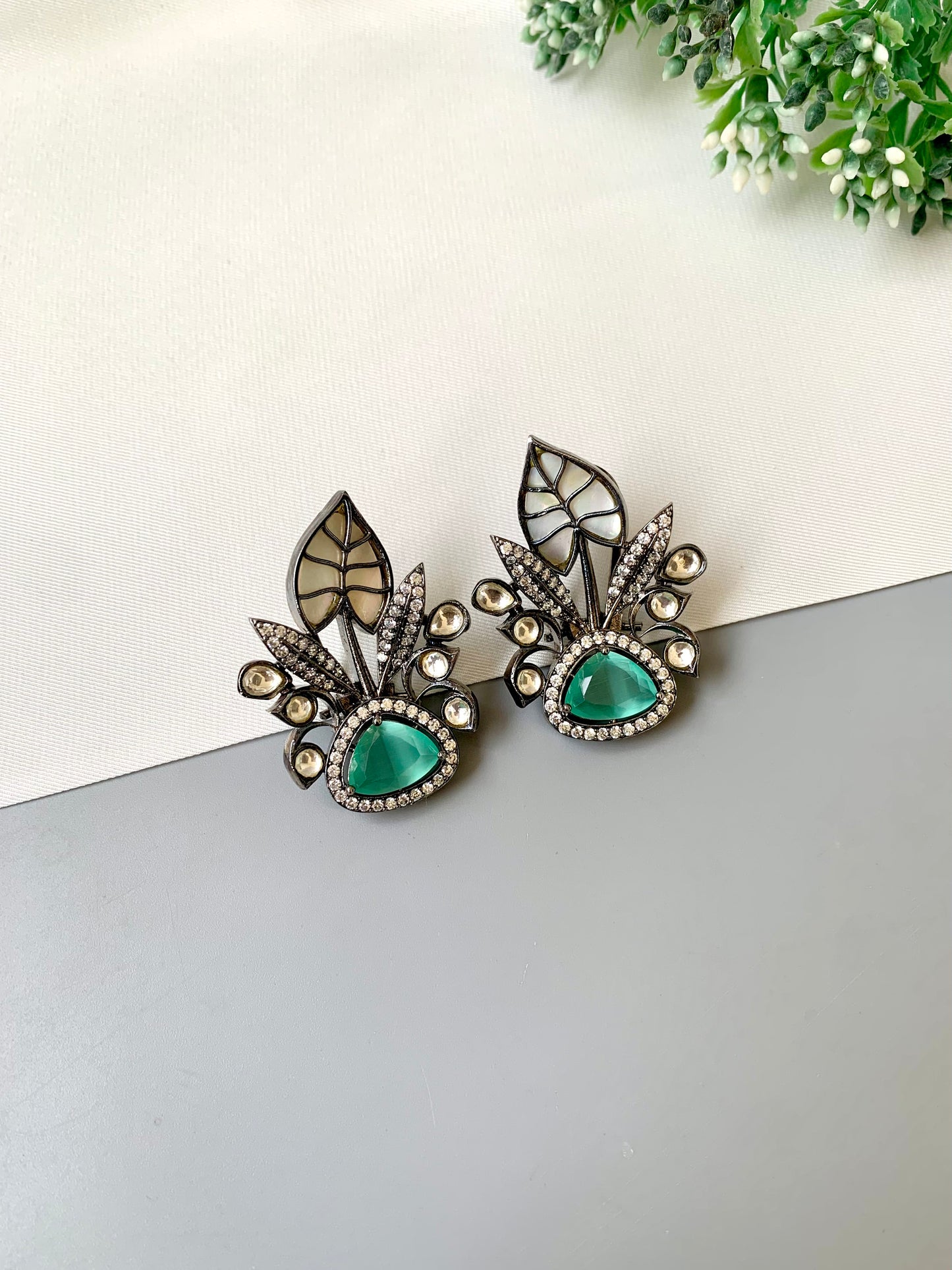 Pair of earrings with green gemstones and decorative elements on a light background