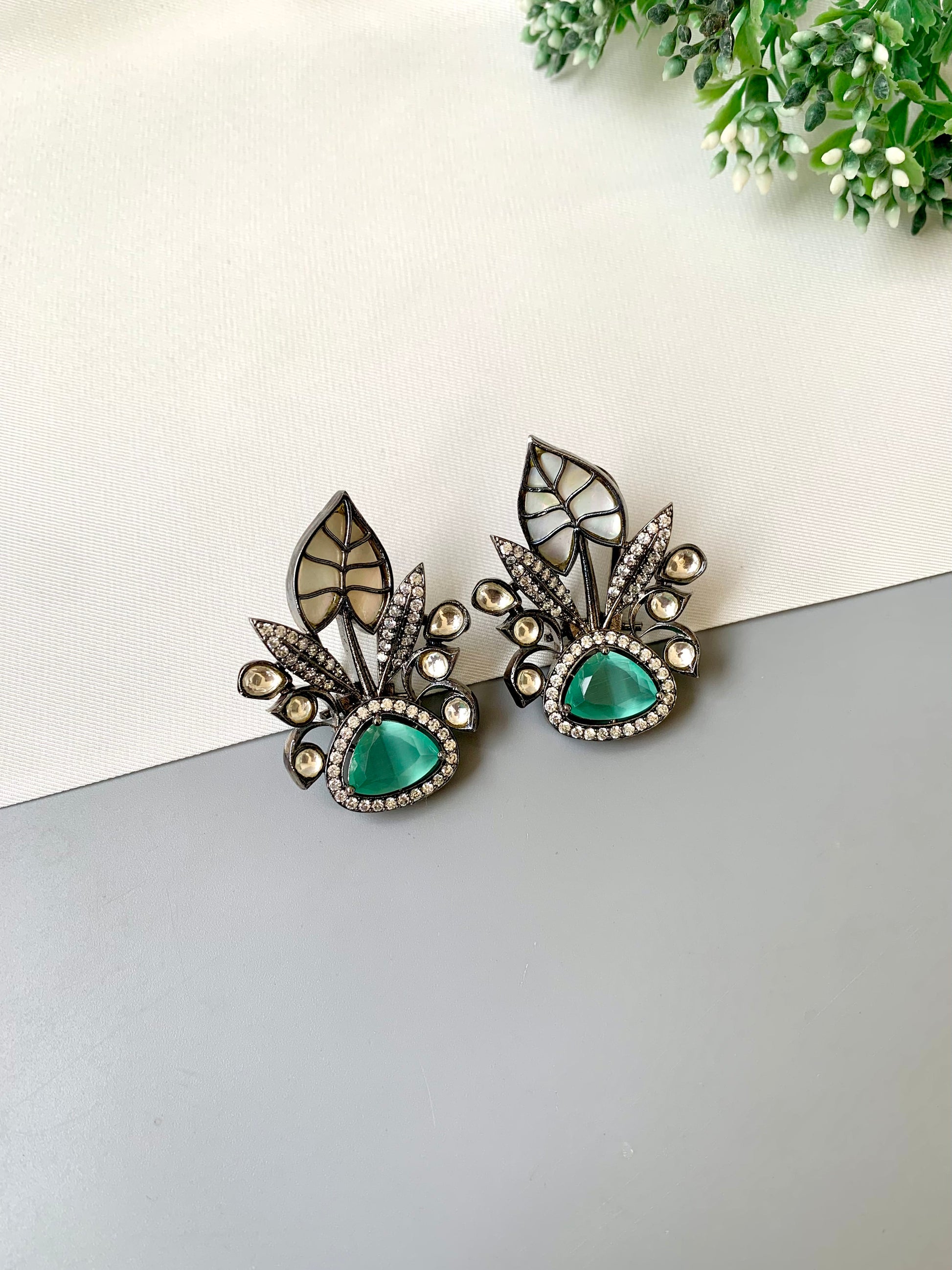 Pair of earrings with green gemstones and decorative elements on a light background