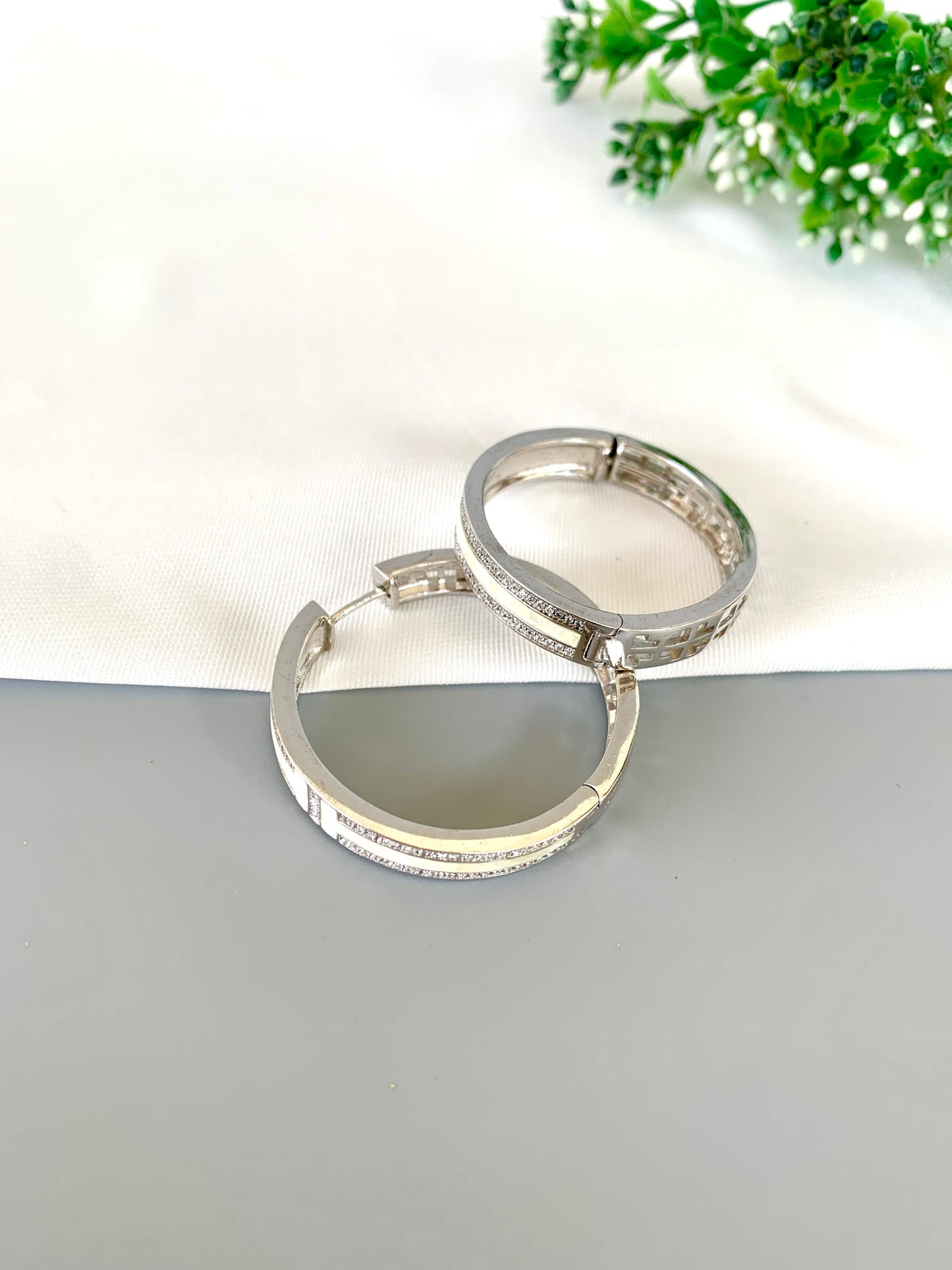 liora-rhodium-hoops-flatlay-zamaljewels.jpg
Flat lay of rhodium-plated hoops on a soft fabric base with greenery decor