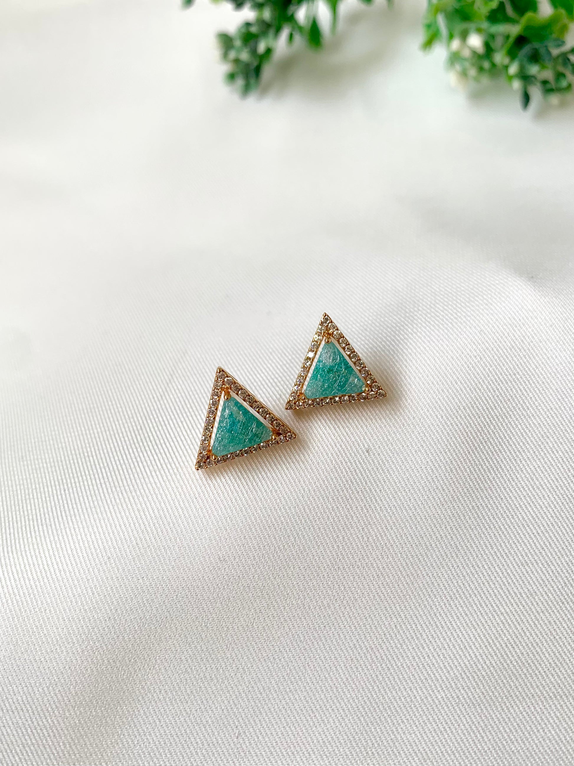 Turquoise triangle earrings on a white fabric background with green leaves.