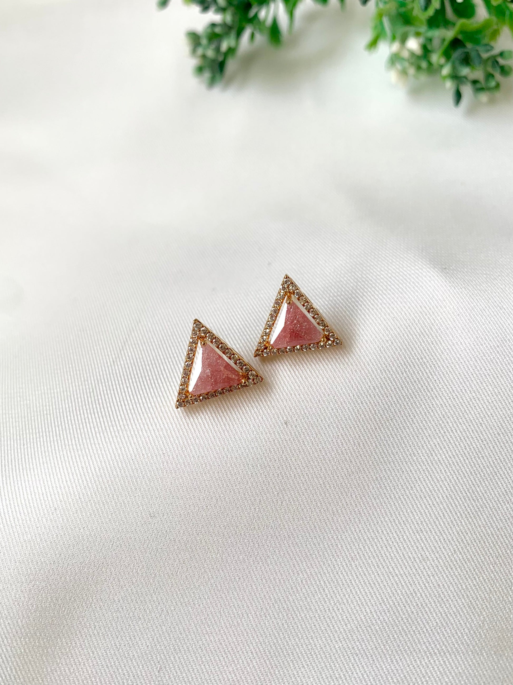 Triangle-shaped earrings with pink center and gold border on a white fabric background.