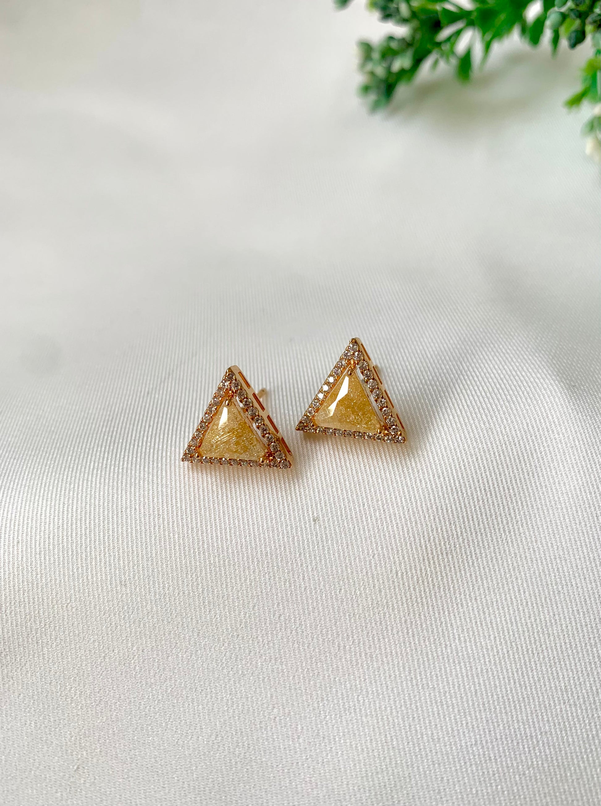 Triangle-shaped earrings on a light fabric background with greenery.
