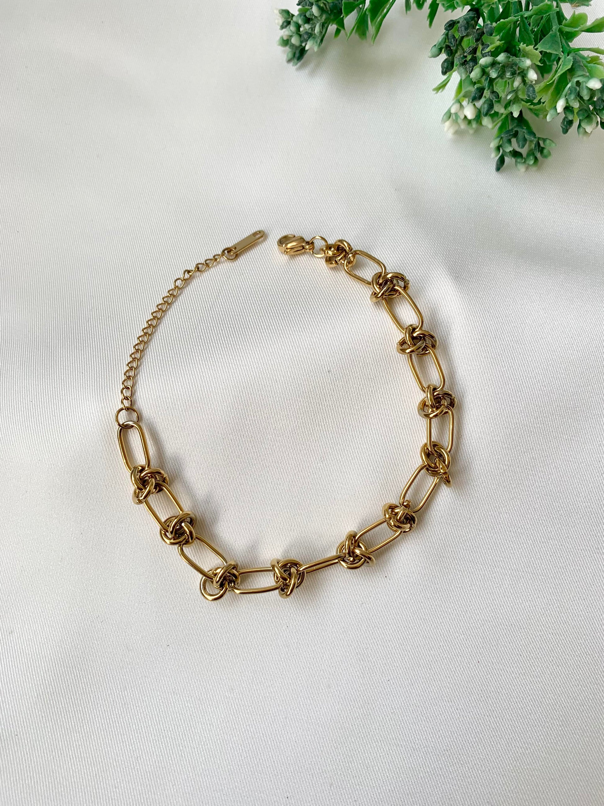 Gold chain bracelet on a white background with greenery