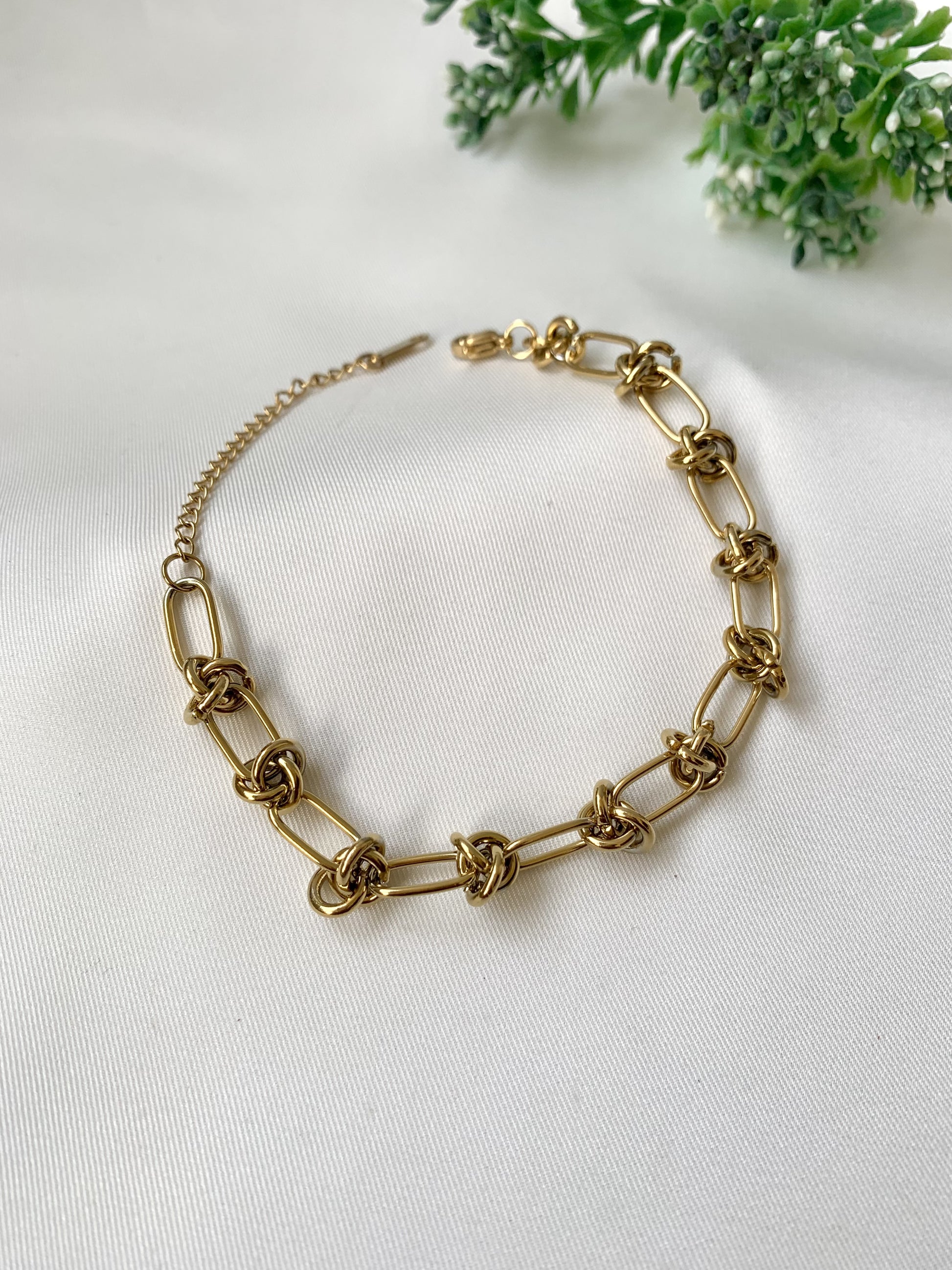 Gold chain necklace on a light gray background with greenery
