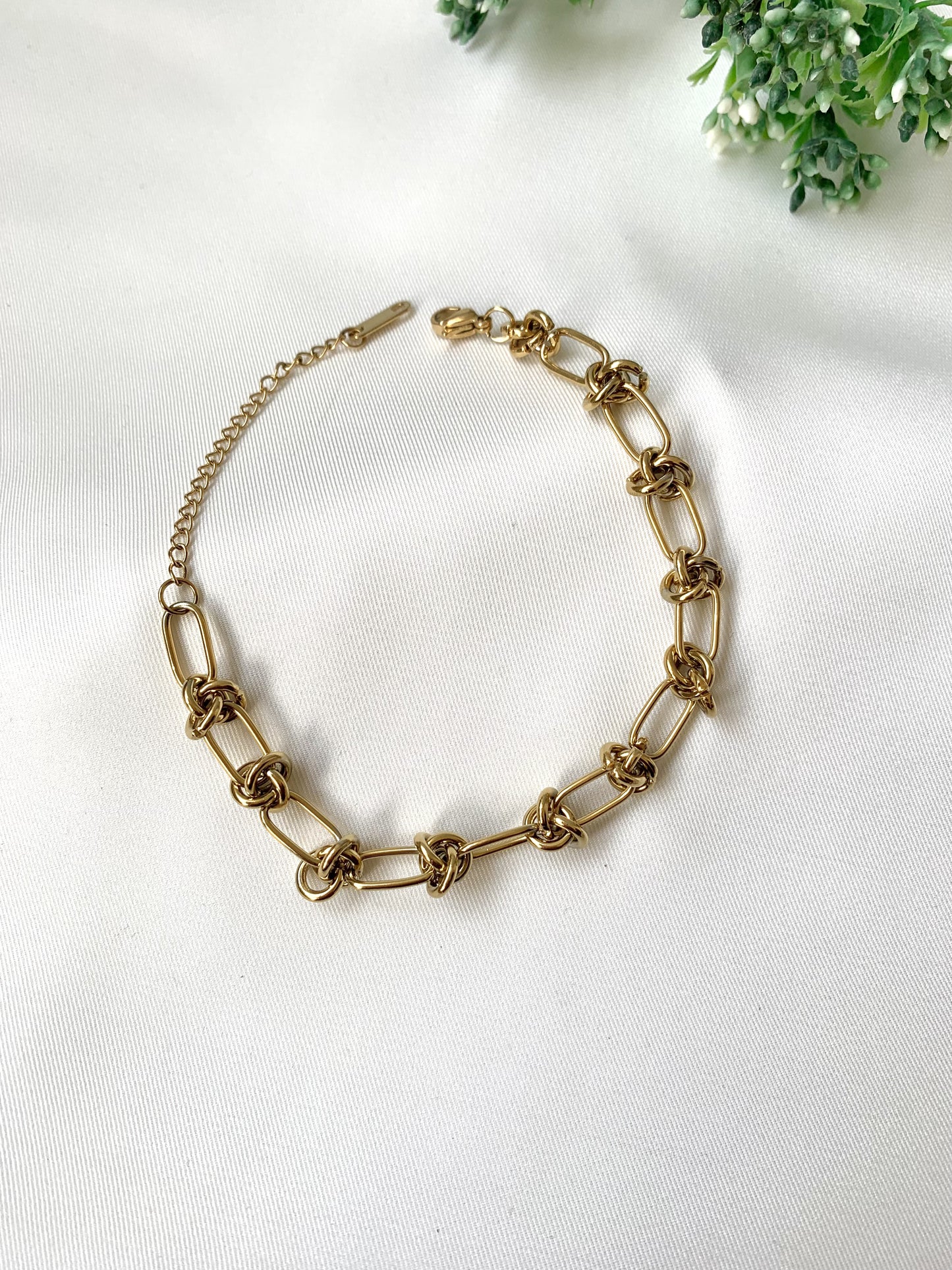 Gold chain necklace on a white background with greenery