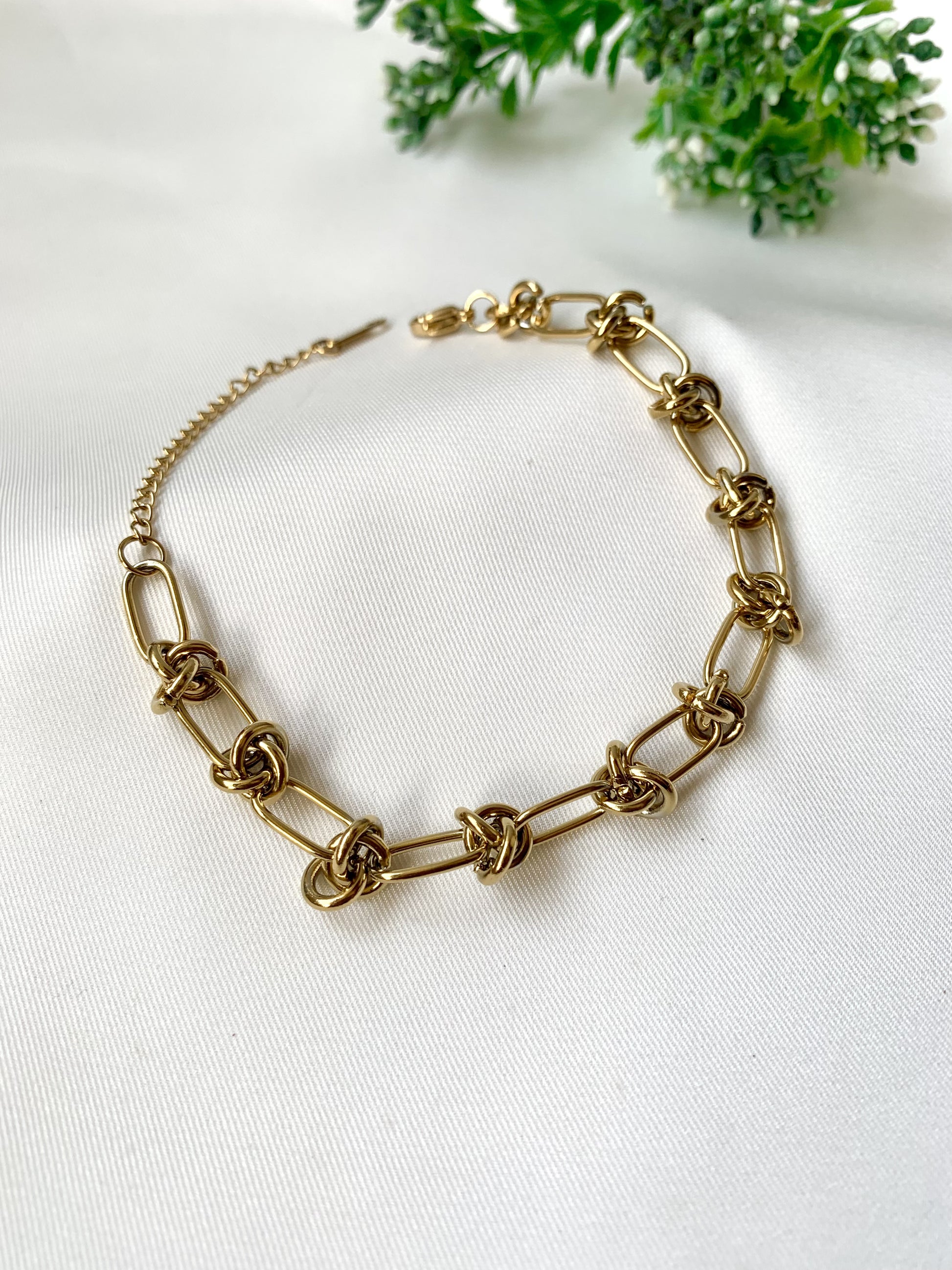 Gold chain necklace on a white fabric background with greenery