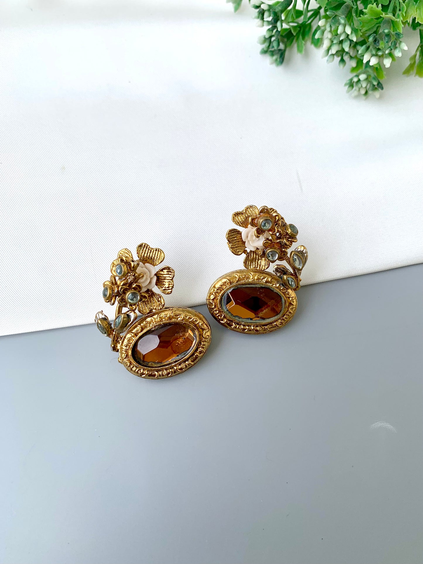 Pair of ornate gold earrings with brown gemstones on a white surface.