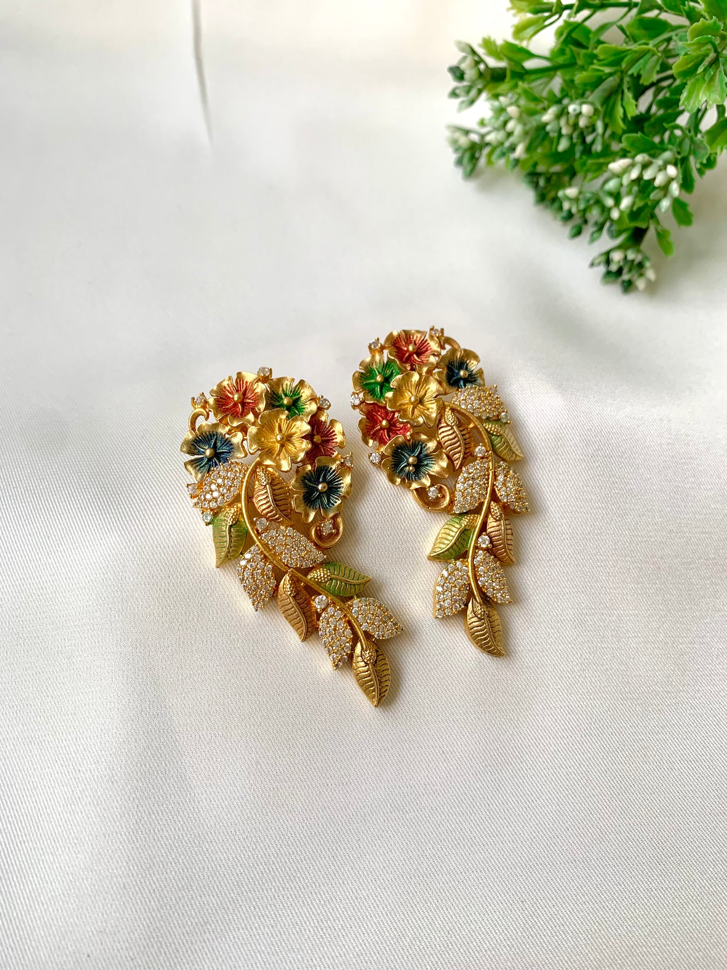 Gold earrings with floral design on a white surface with greenery in the background