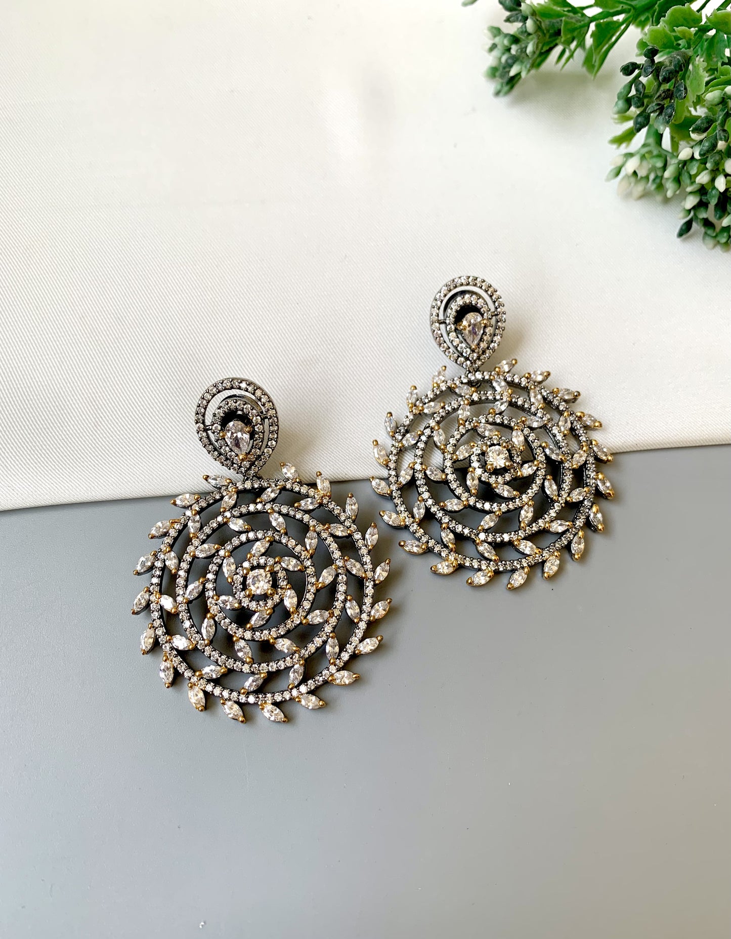 Pair of ornate earrings on a light surface with greenery in the background