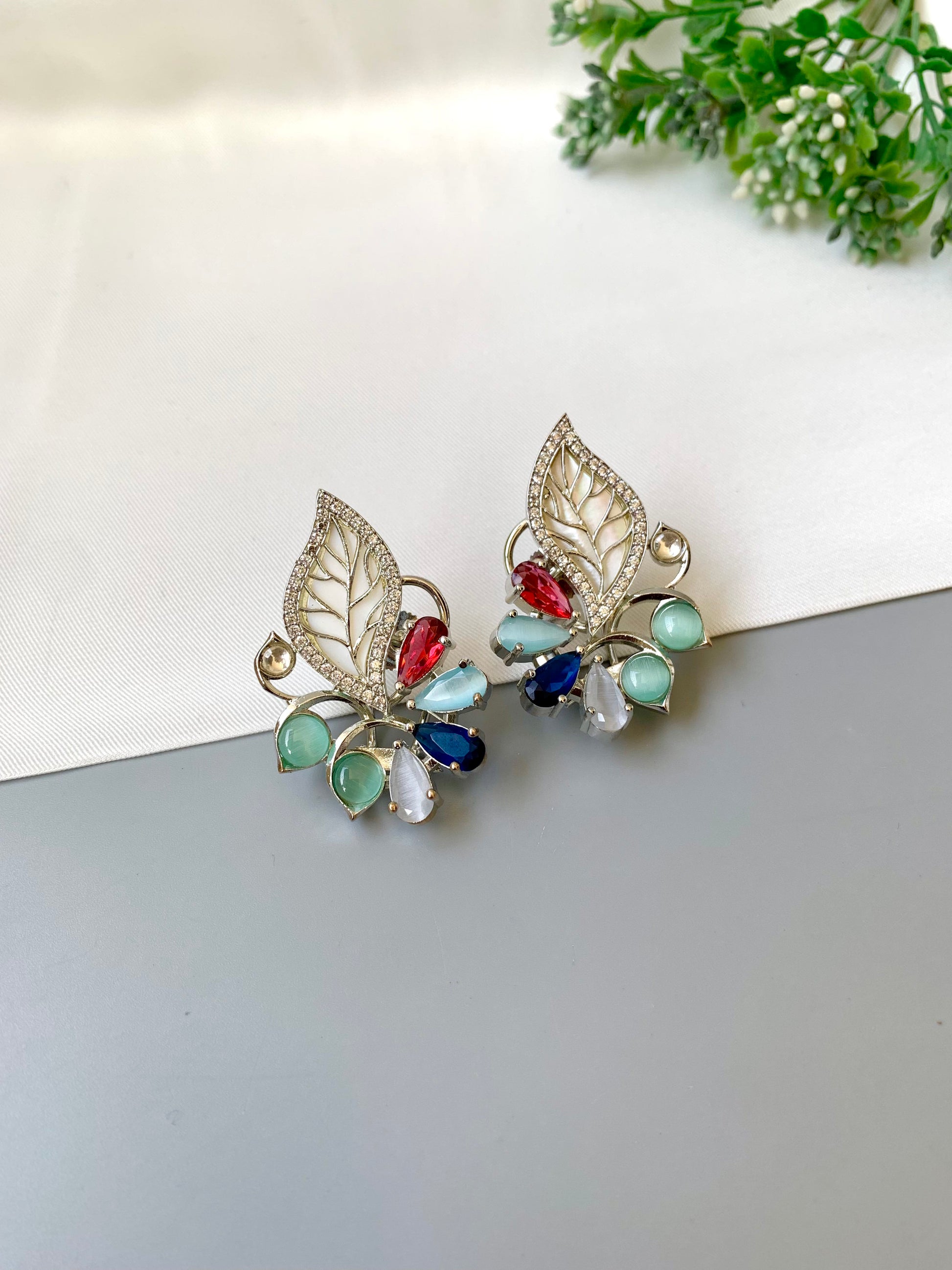 Pair of earrings with leaf design and colorful gemstones on a light background