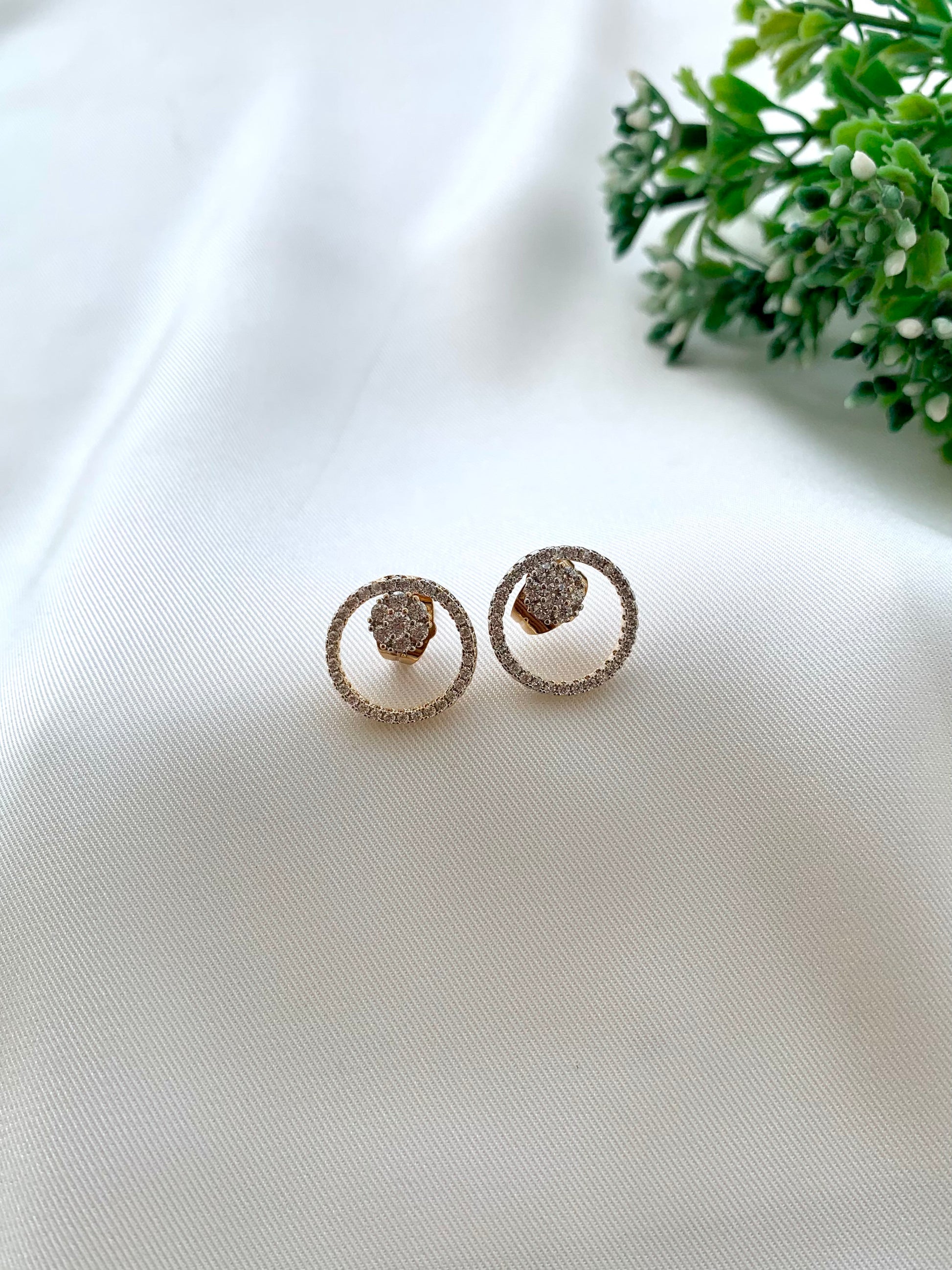 Pair of silver earrings on a white fabric background with green leaves.