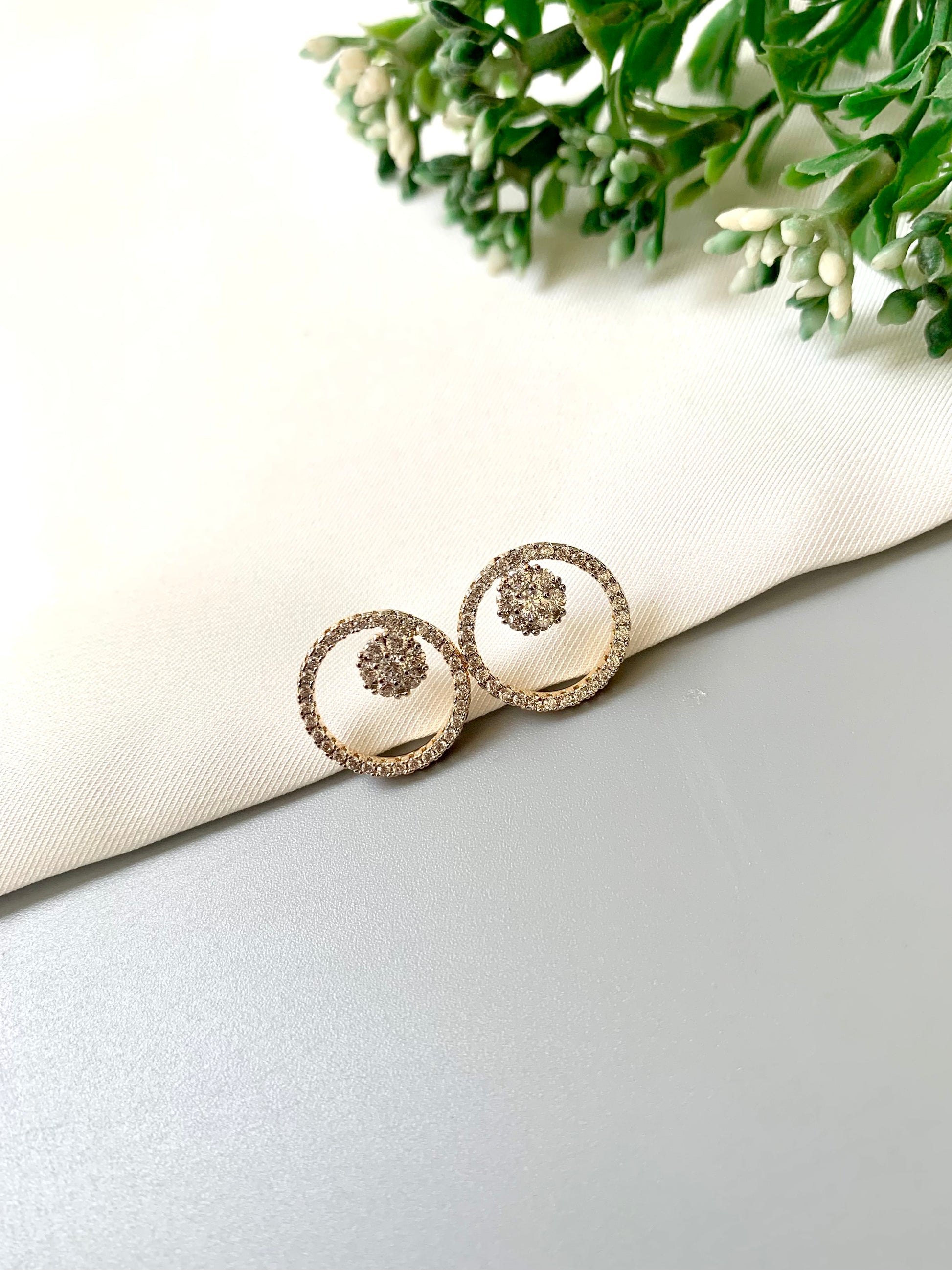 Pair of silver earrings on a white fabric background with green leaves.