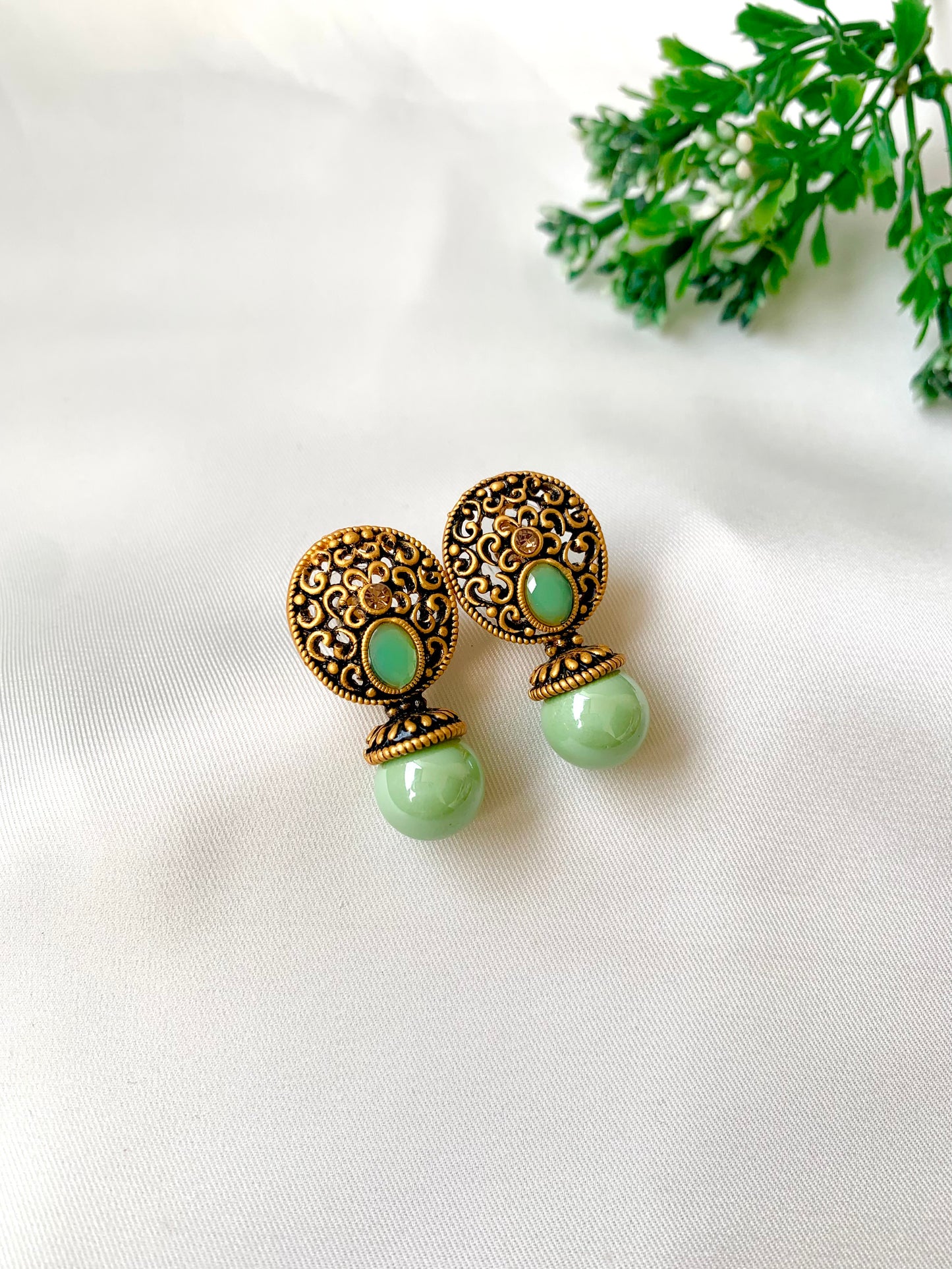 Pair of gold and green earrings on a white background with green leaves.