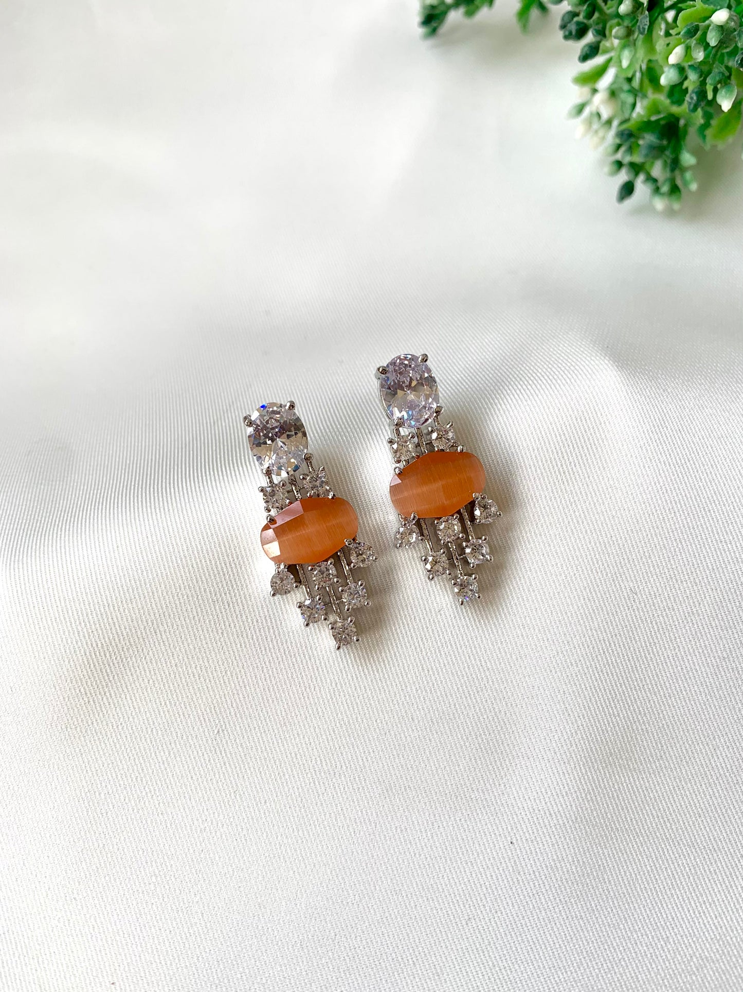 Pair of earrings with orange stones on a white fabric background