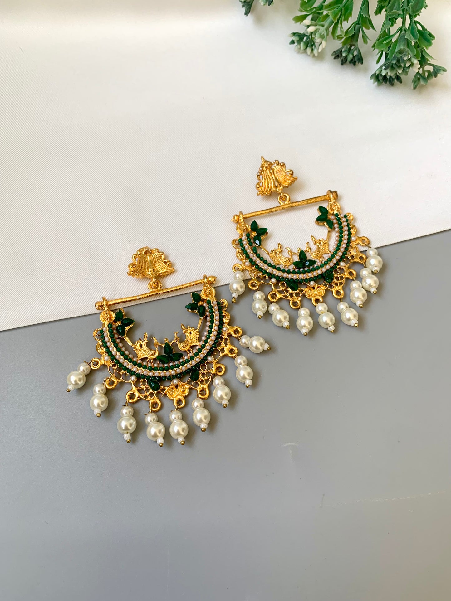 Ornate gold and green earrings with pearl drops on a light gray surface.