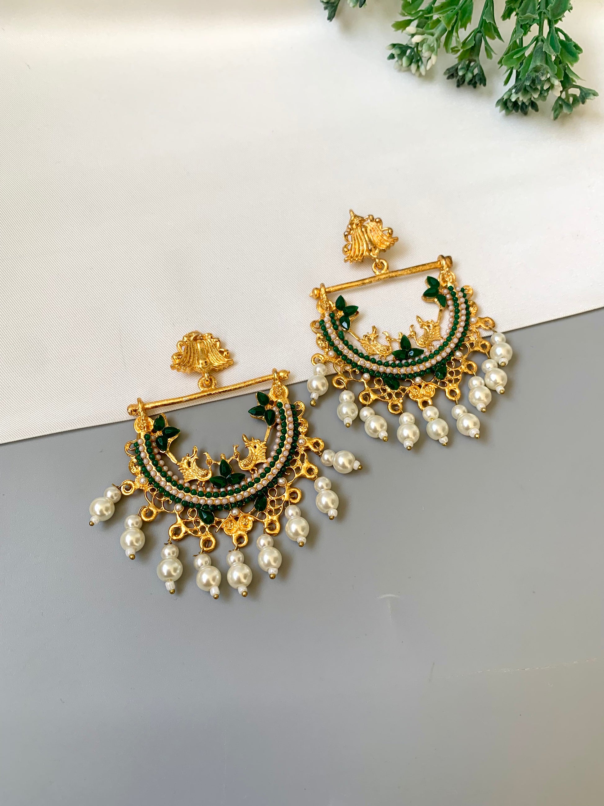 Ornate gold and green earrings with pearl drops on a light gray surface.