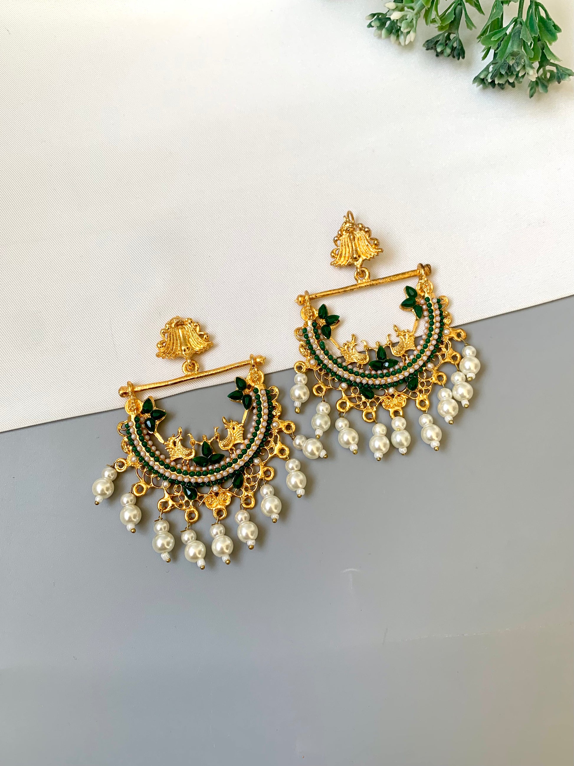 Gold and green earrings with pearl accents on a white surface.