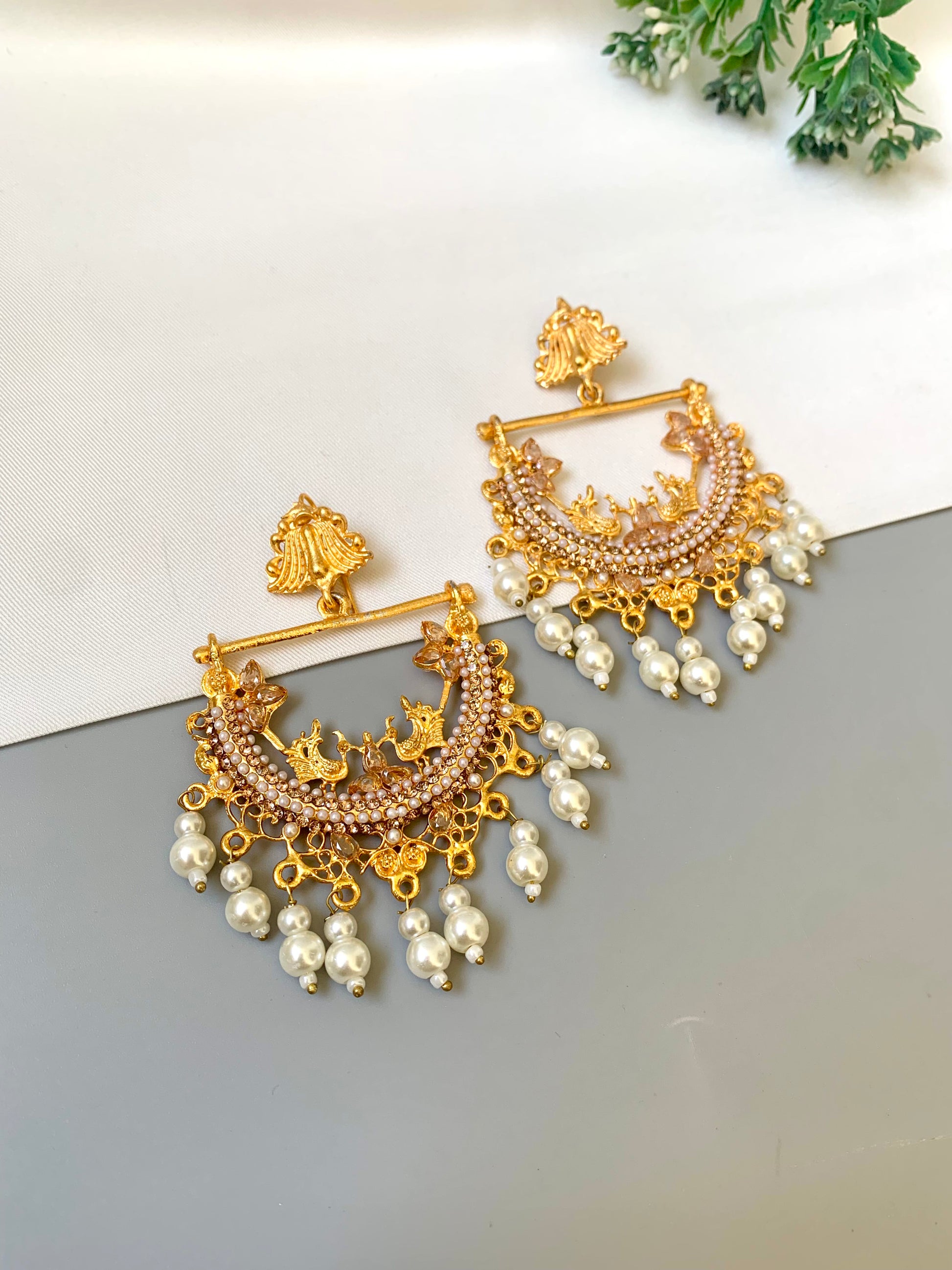 Gold and pearl earrings on a light gray surface with a white background