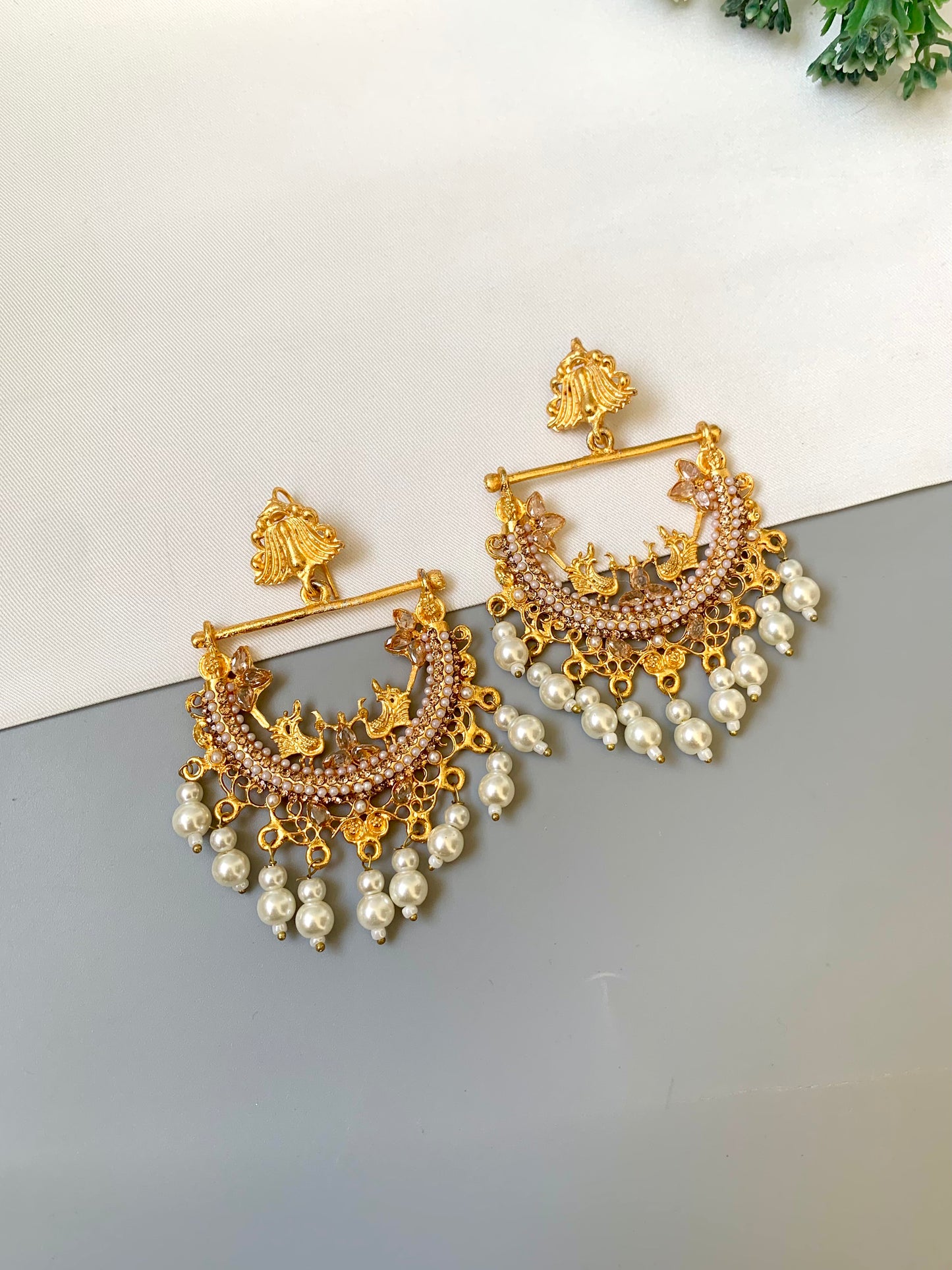 Gold and pearl earrings on a reflective surface with a light background