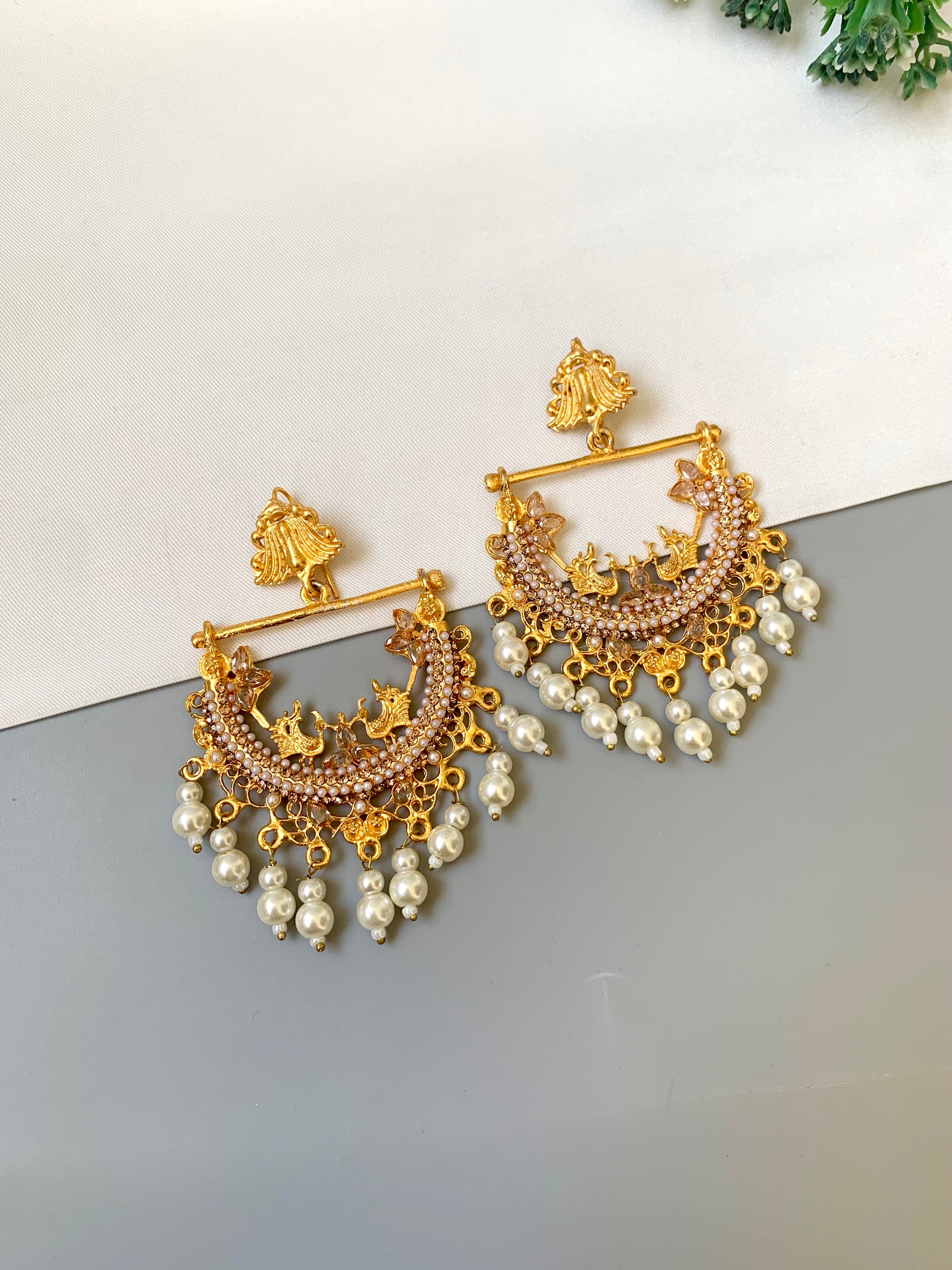 Gold and pearl earrings on a reflective surface with a light background