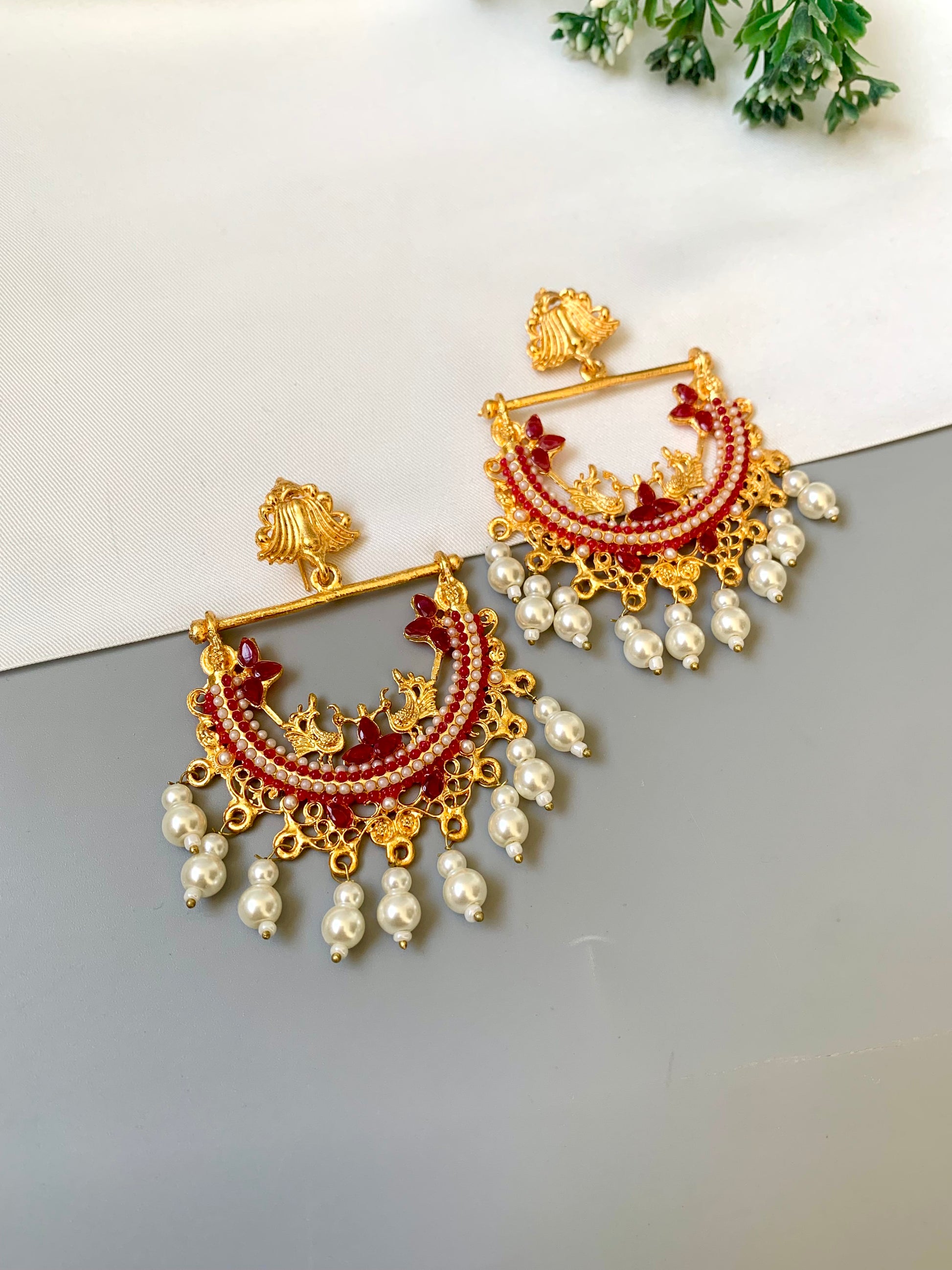 Ornate gold and red earrings with pearl accents on a white and gray gradient background.