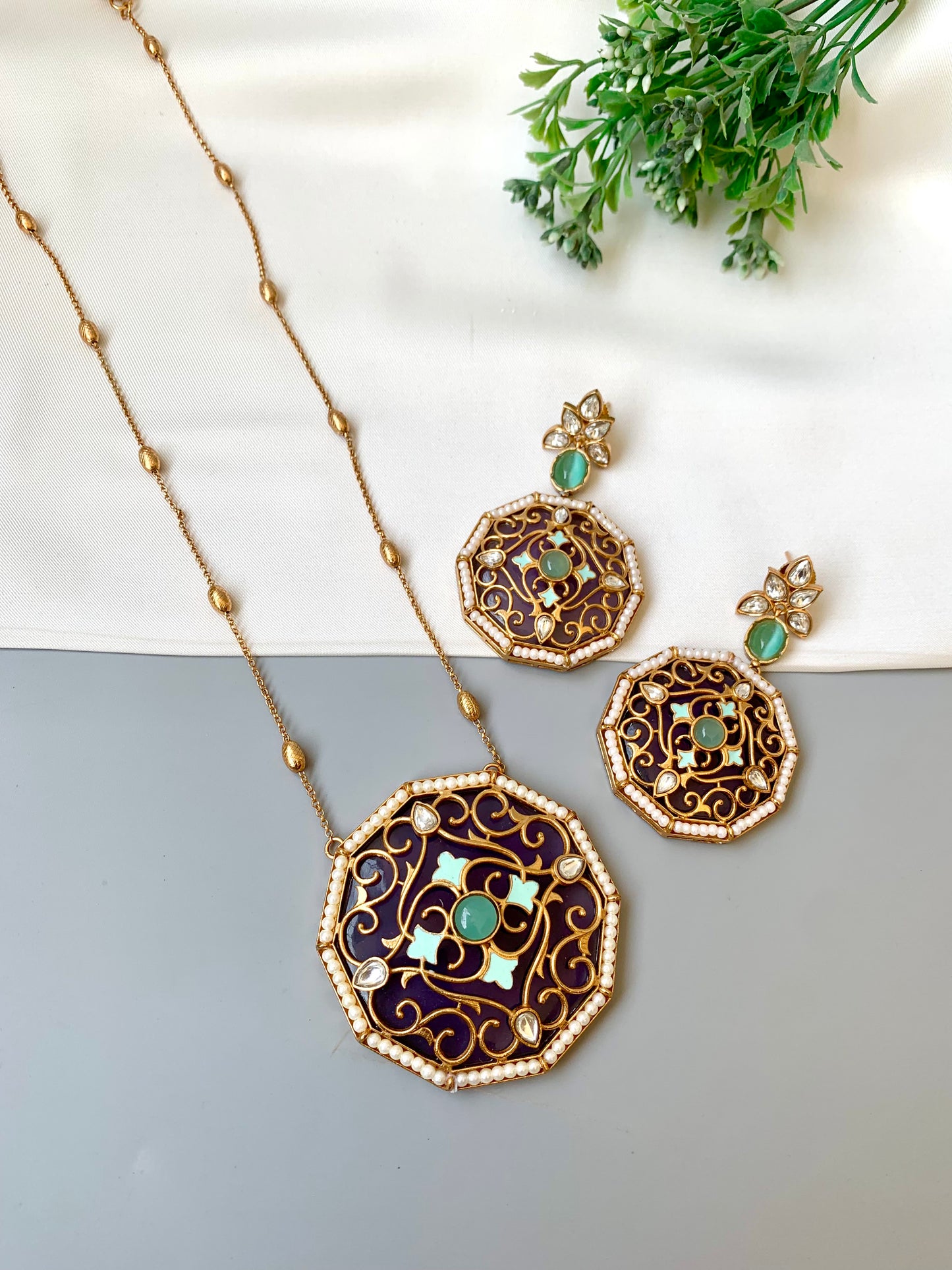 Ornate necklace and earrings with green gemstones on a neutral background