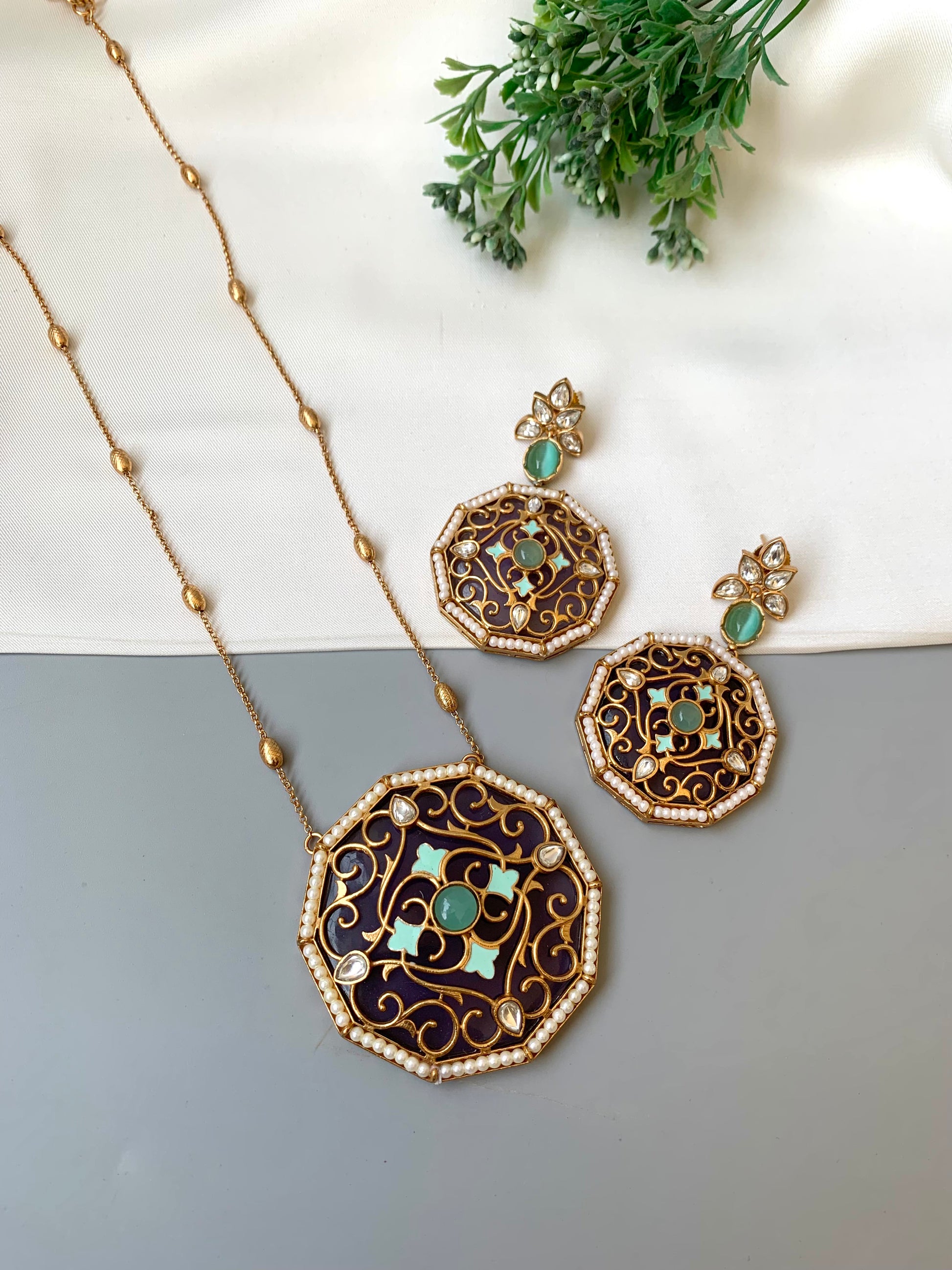 Ornate necklace and earrings with green gemstones on a gray surface.