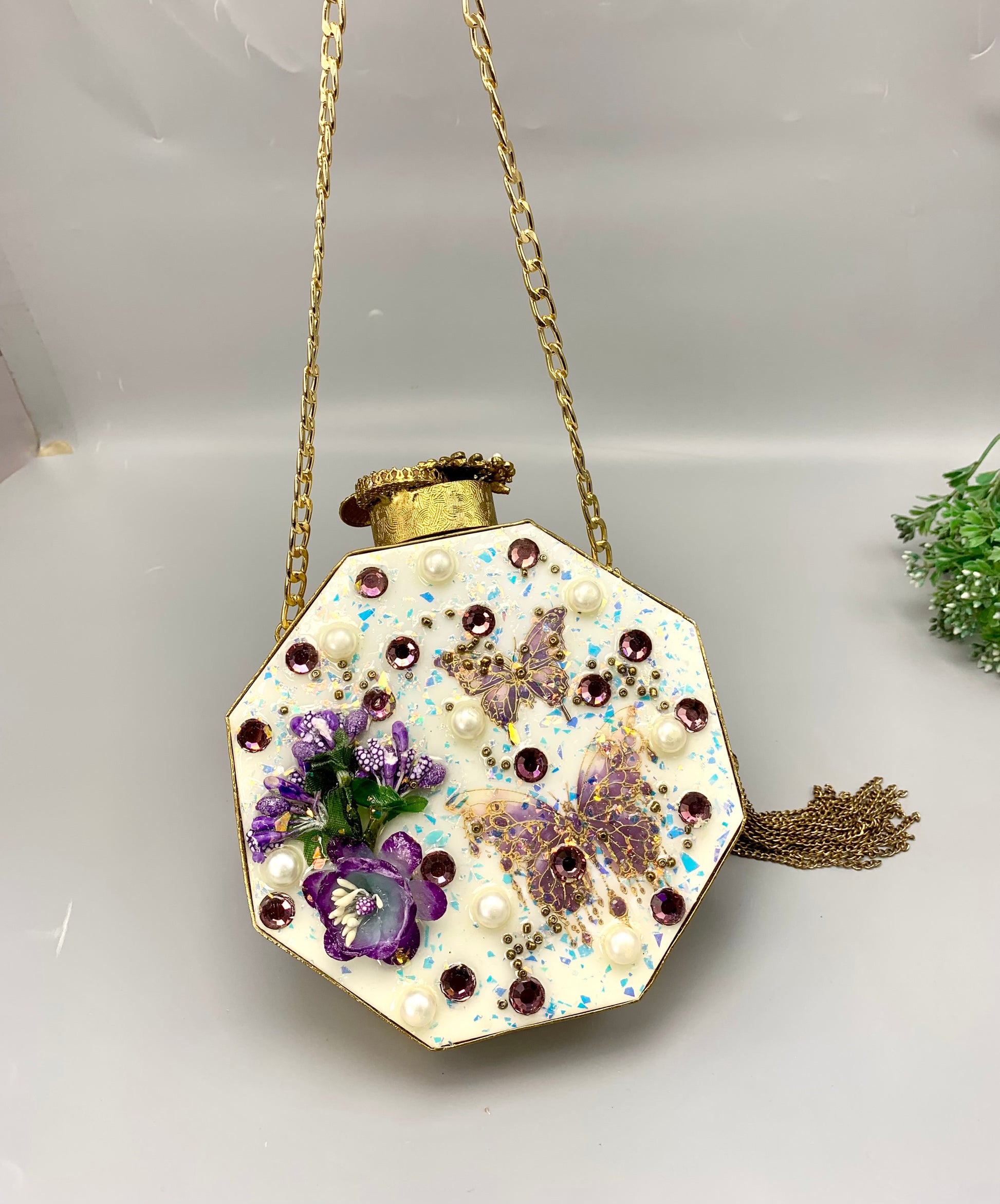 Decorative hexagonal pendant with floral elements and pearls on a gold chain against a white background.
