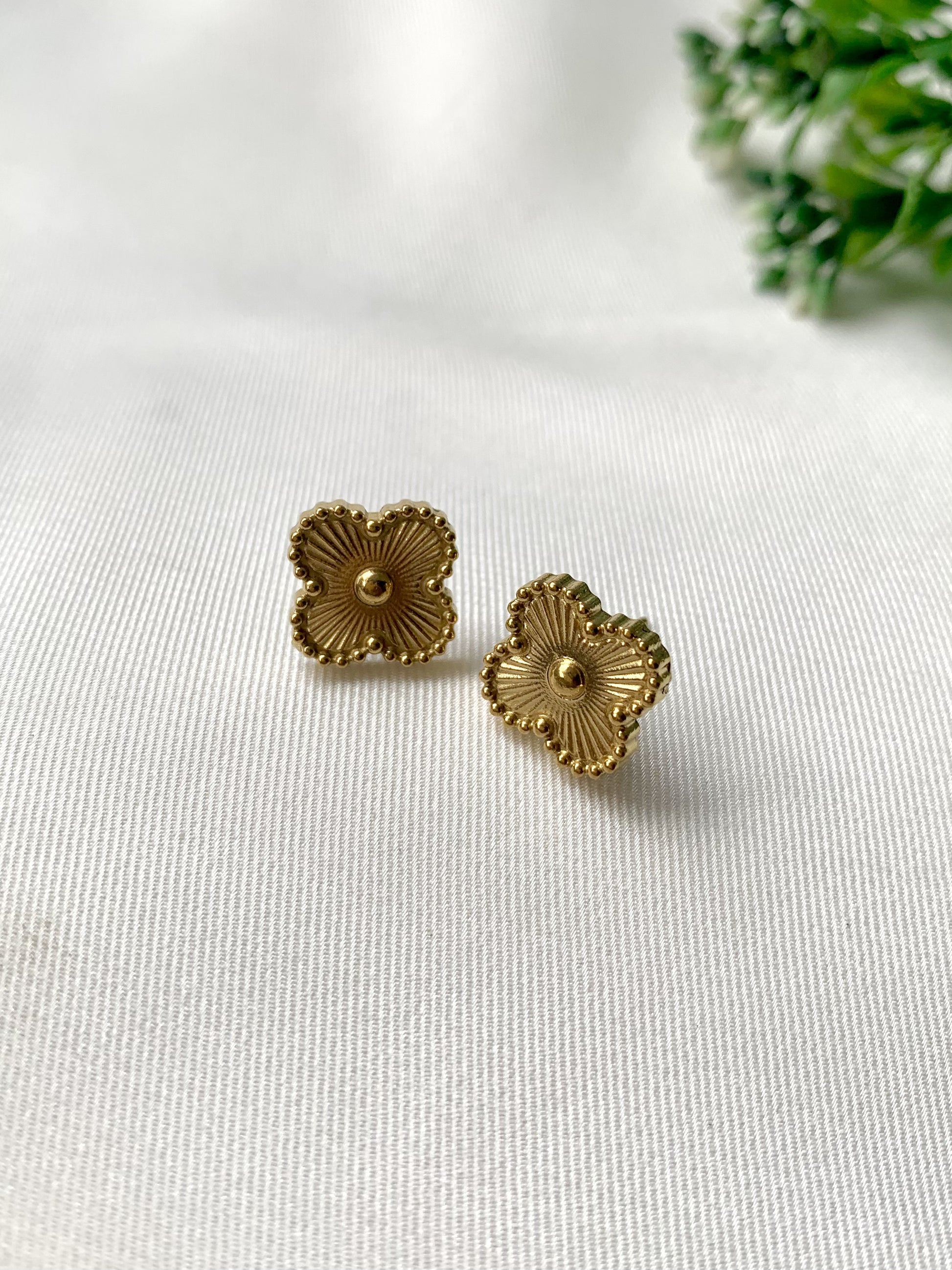 Pair of gold floral earrings on a white fabric background