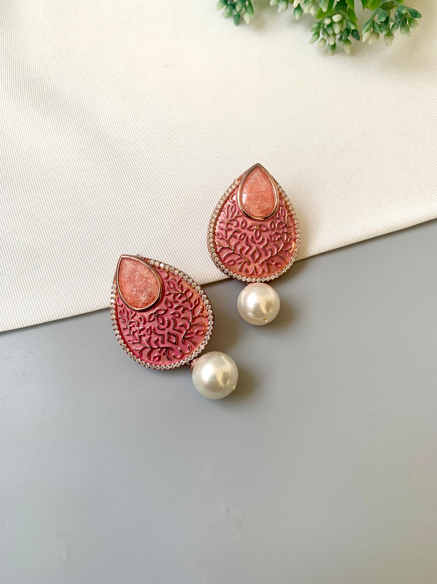 Pair of pink textured earrings with pearl accents on a light gray surface.