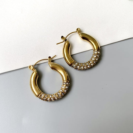 Gold-plated stainless steel crystal-accented hoop earrings with a sleek, classic design, laid out on a neutral background.