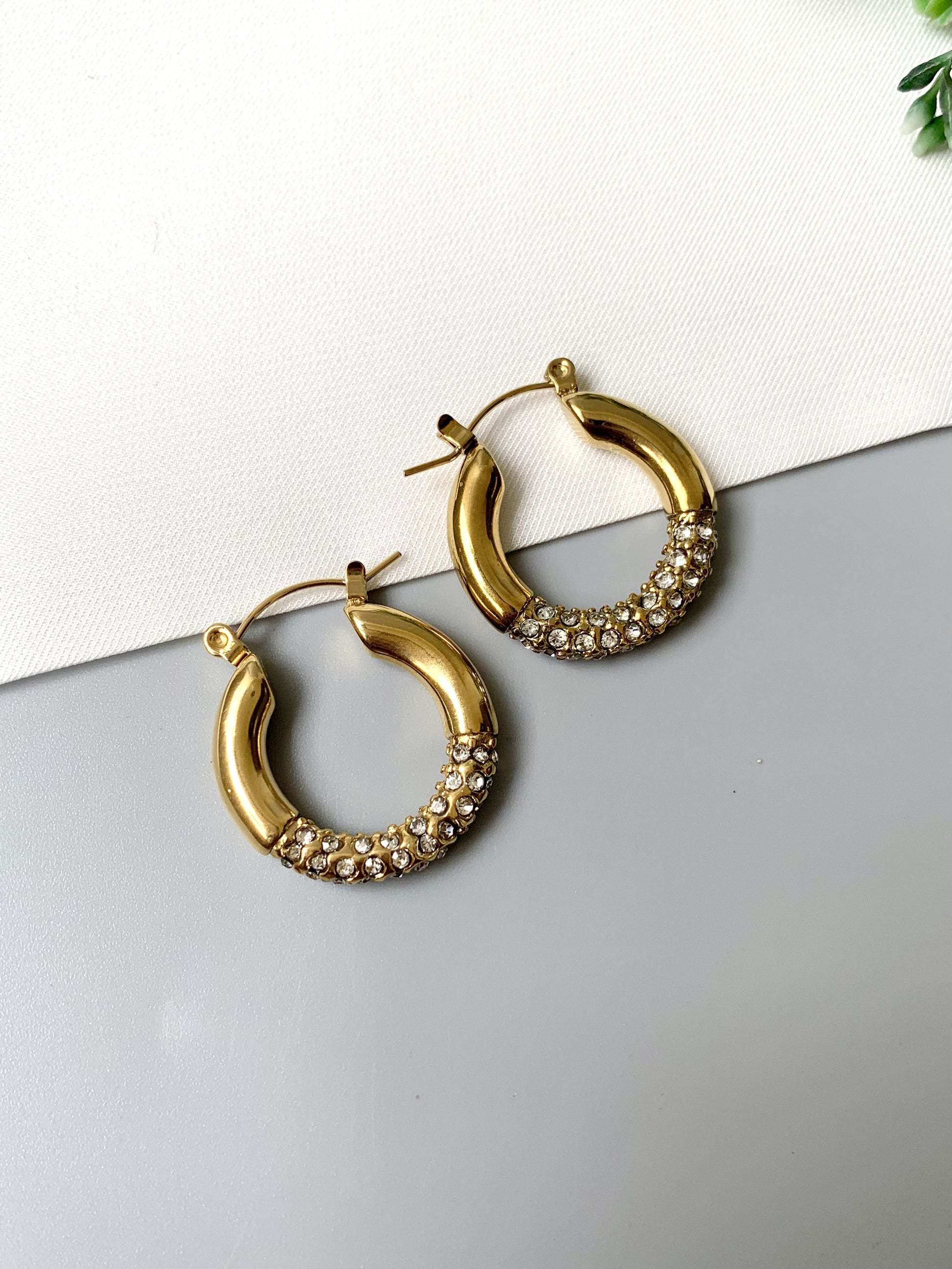 Gold-plated stainless steel crystal-accented hoop earrings with a sleek, classic design, laid out on a neutral background.