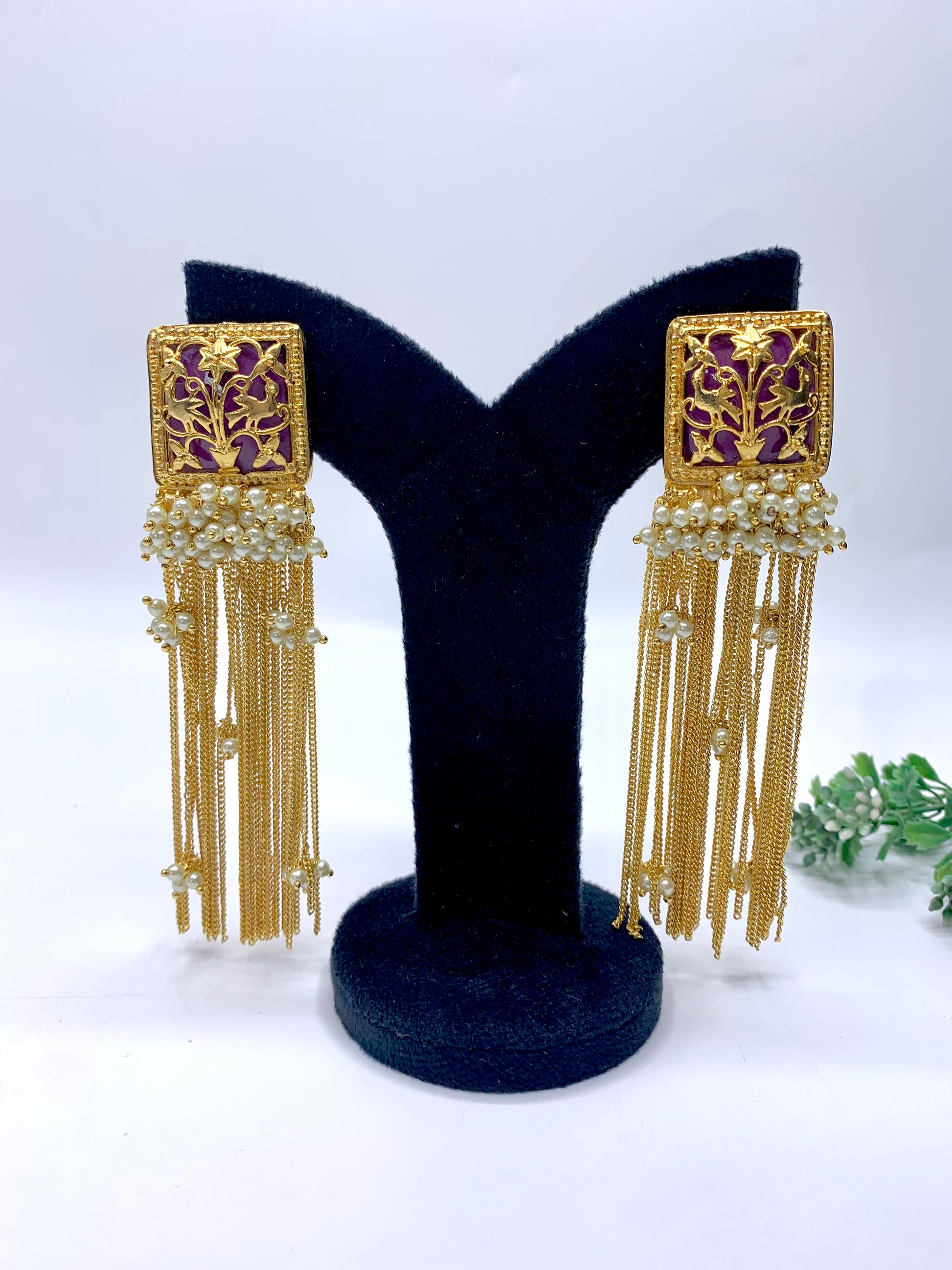 Gold-framed earrings with tassels on a black stand against a white background