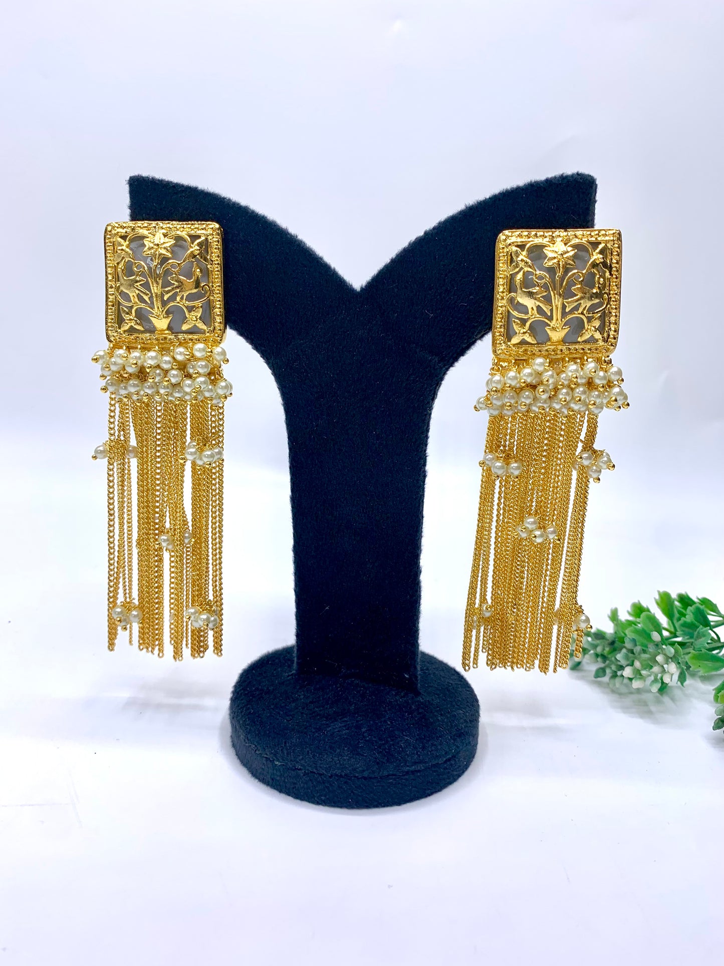 Gold earrings with tassels on a black stand against a white background