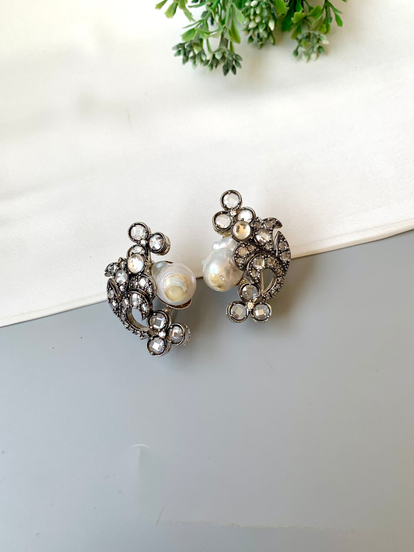 Pair of ornate earrings with pearls on a white surface.