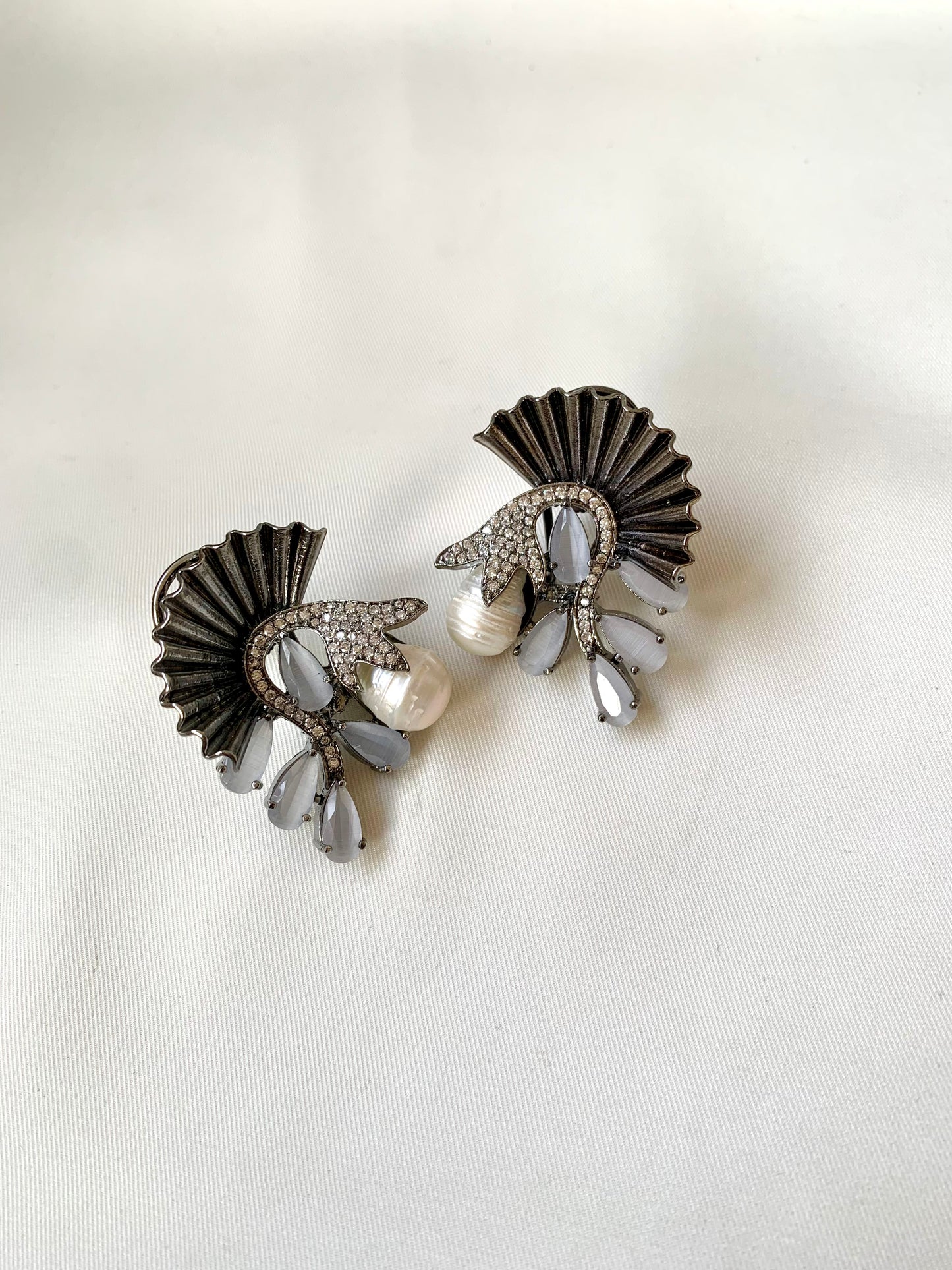 Pair of decorative earrings with fan-like design and pearl accents on a white background