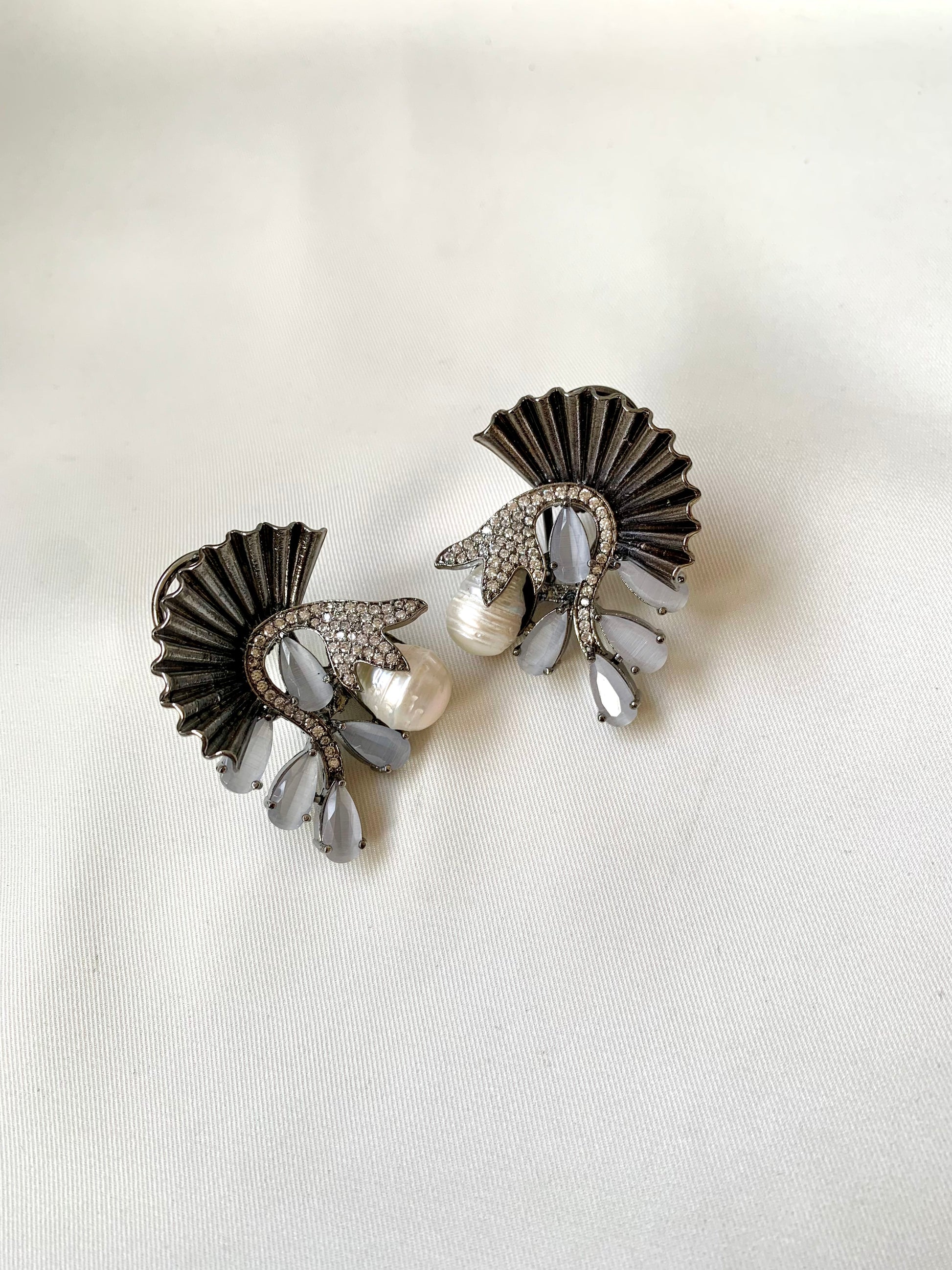 Pair of decorative earrings with fan-like design and pearl accents on a white background
