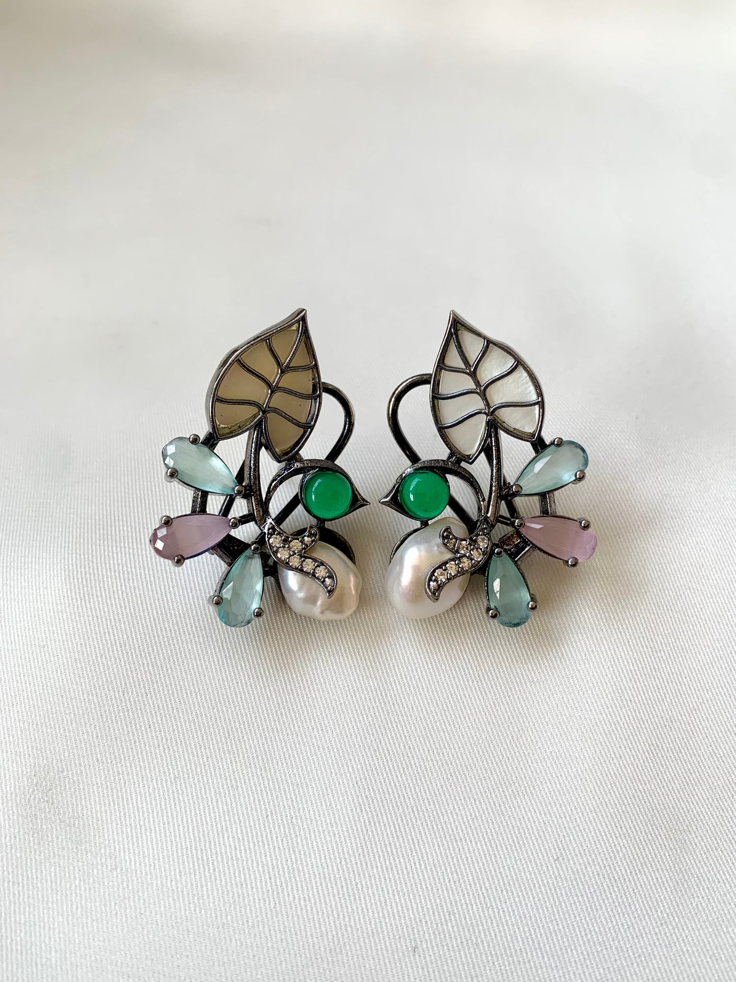 Pair of earrings with leaf design and gemstones on a white background