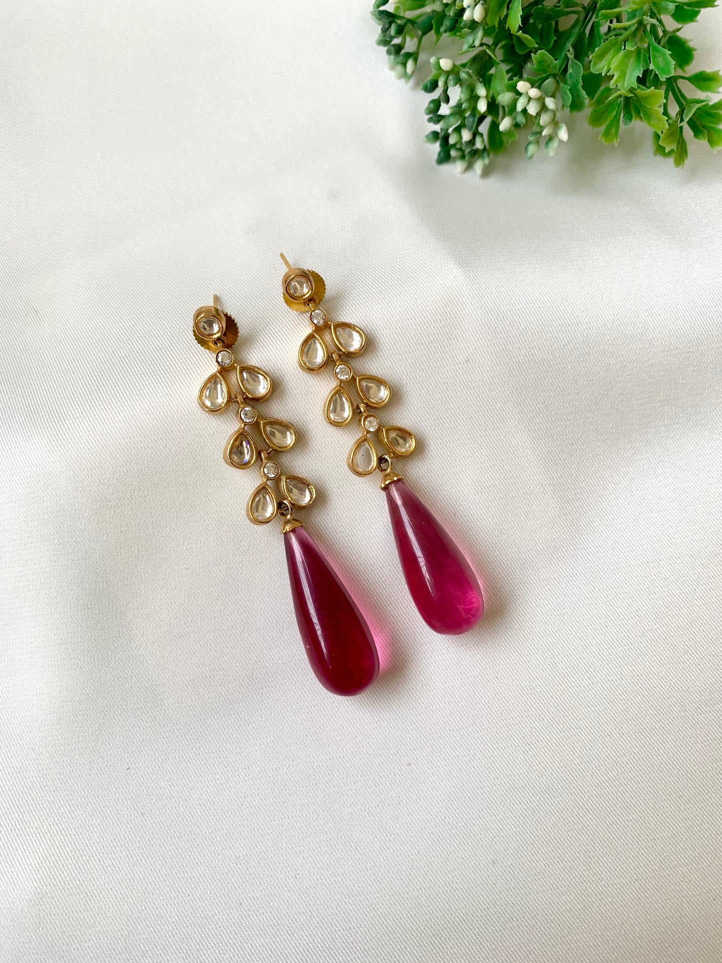 Gold and red teardrop earrings on a light fabric background with greenery.