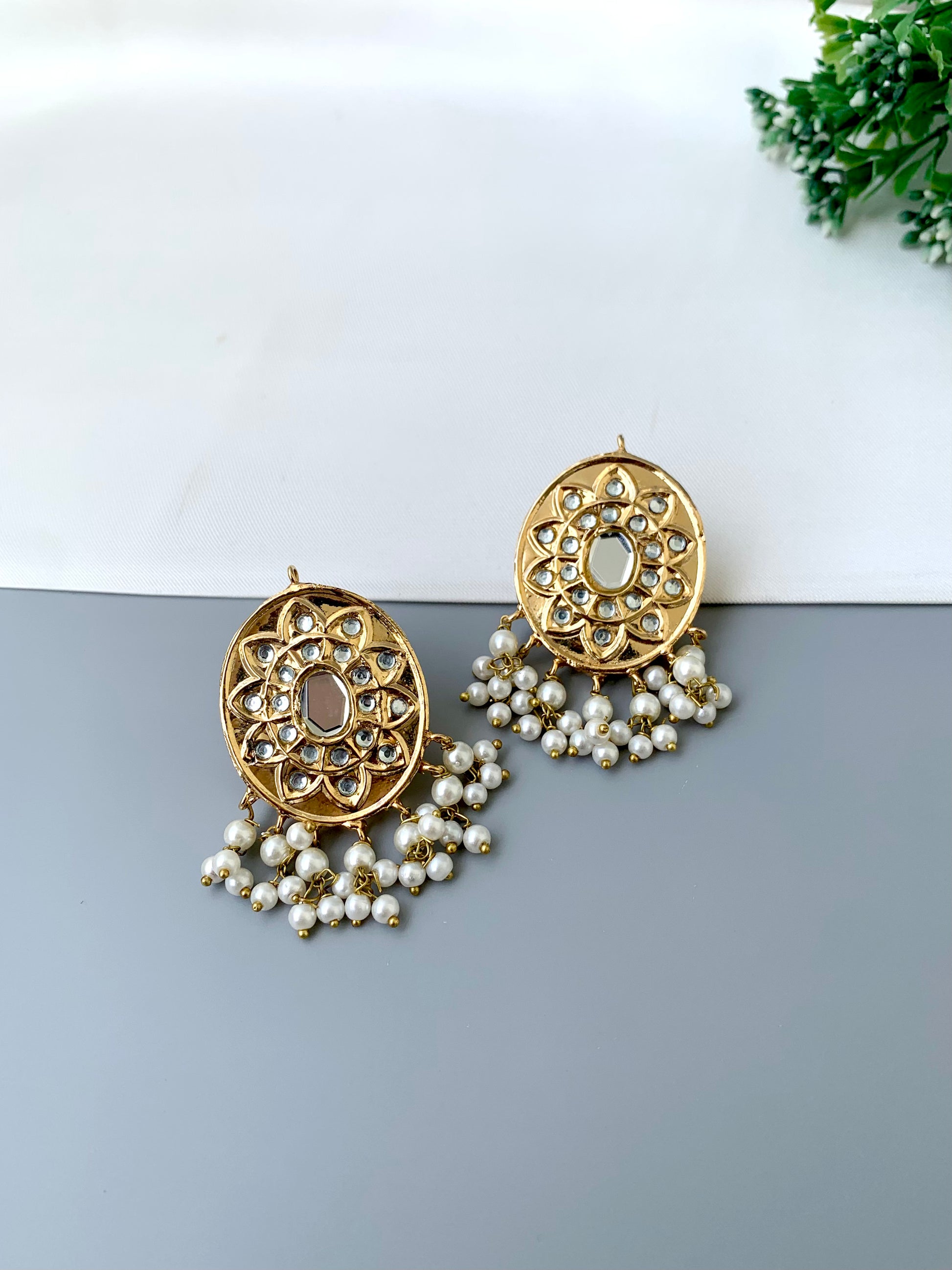 Gold earrings with pearl drops on a white and gray gradient background