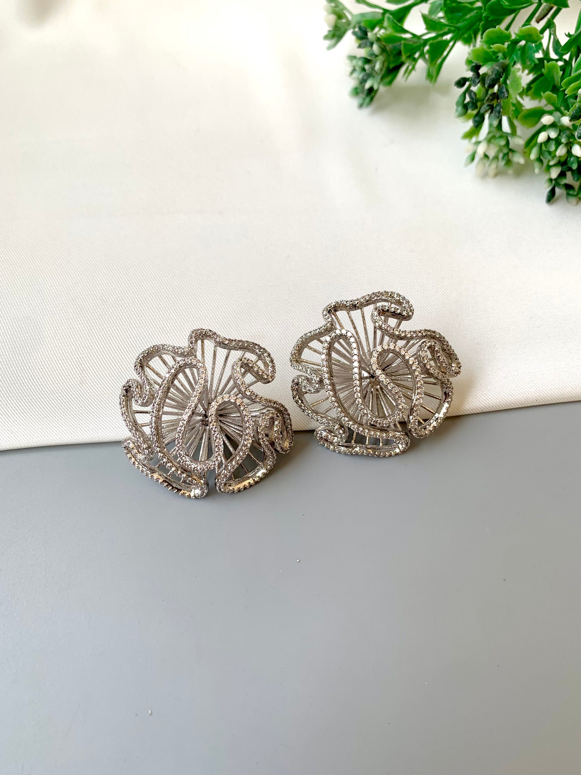 Silver earrings on a light gray surface with a white and green background