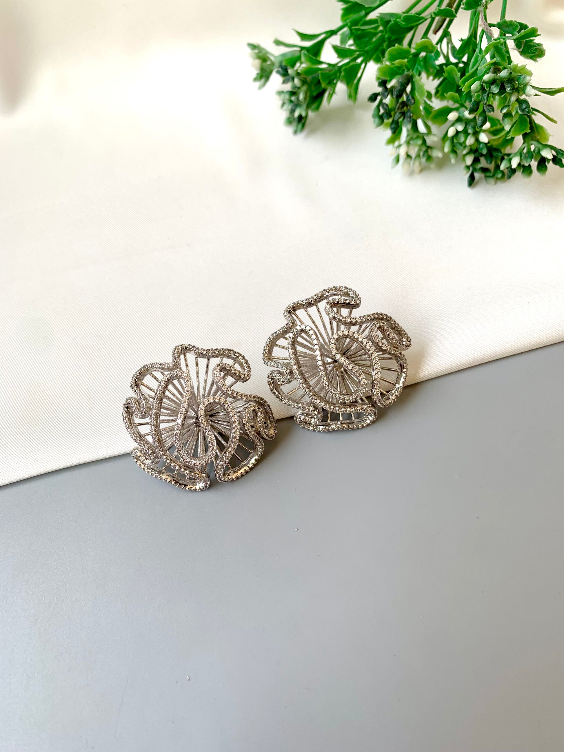 Silver earrings on a white surface with greenery in the background
