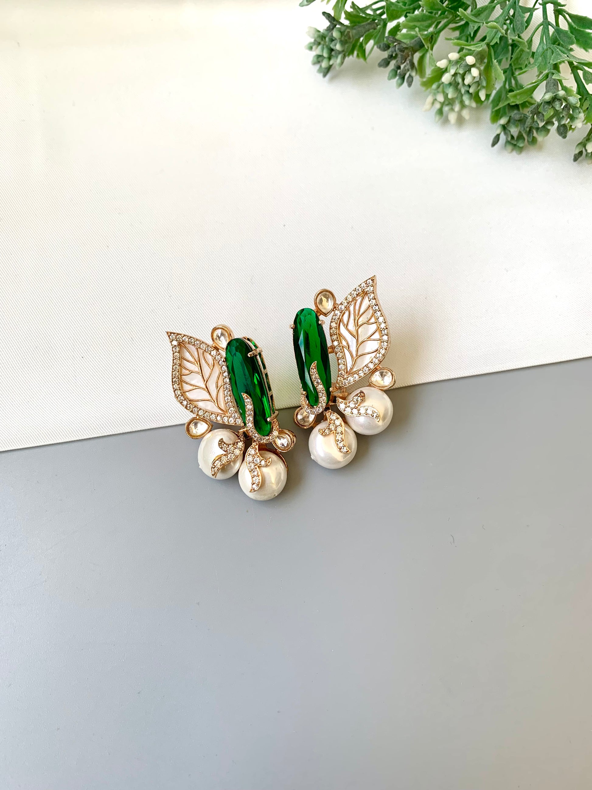 Butterfly-shaped earrings with green and gold details on a white and gray background